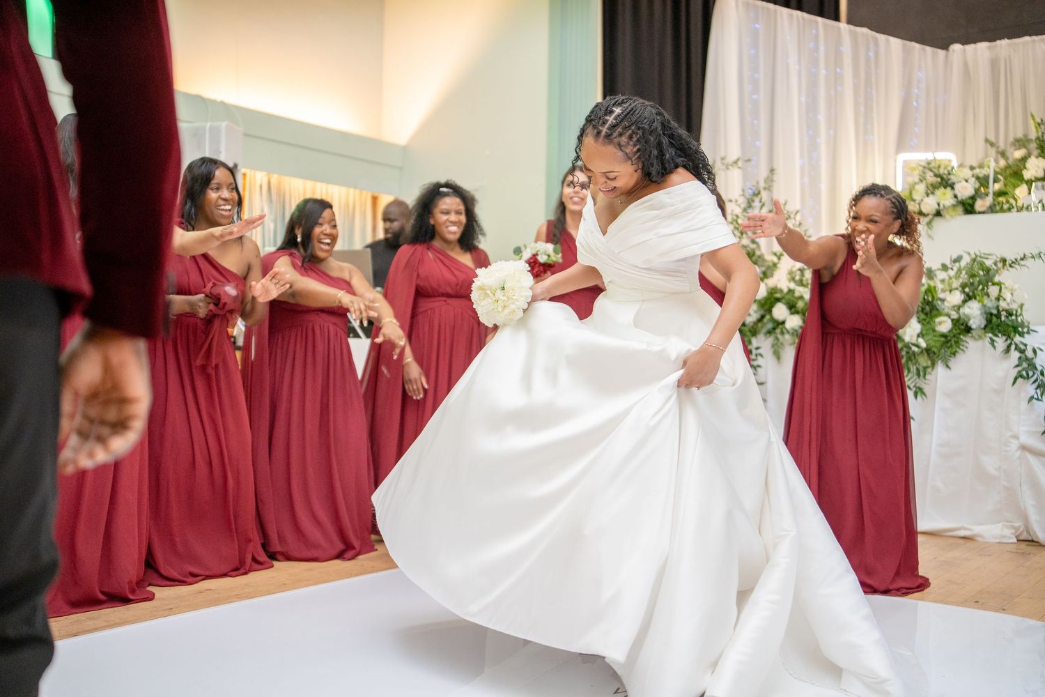 Bride in white gown dances joyfully as bridesmaids in red dresses celebrate at elegant wedding reception.