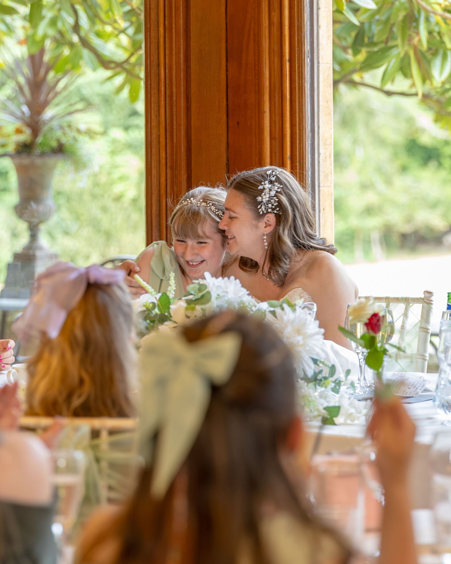 Bride laughing with young flower girl at elegant wedding reception table decorated with white flowers.