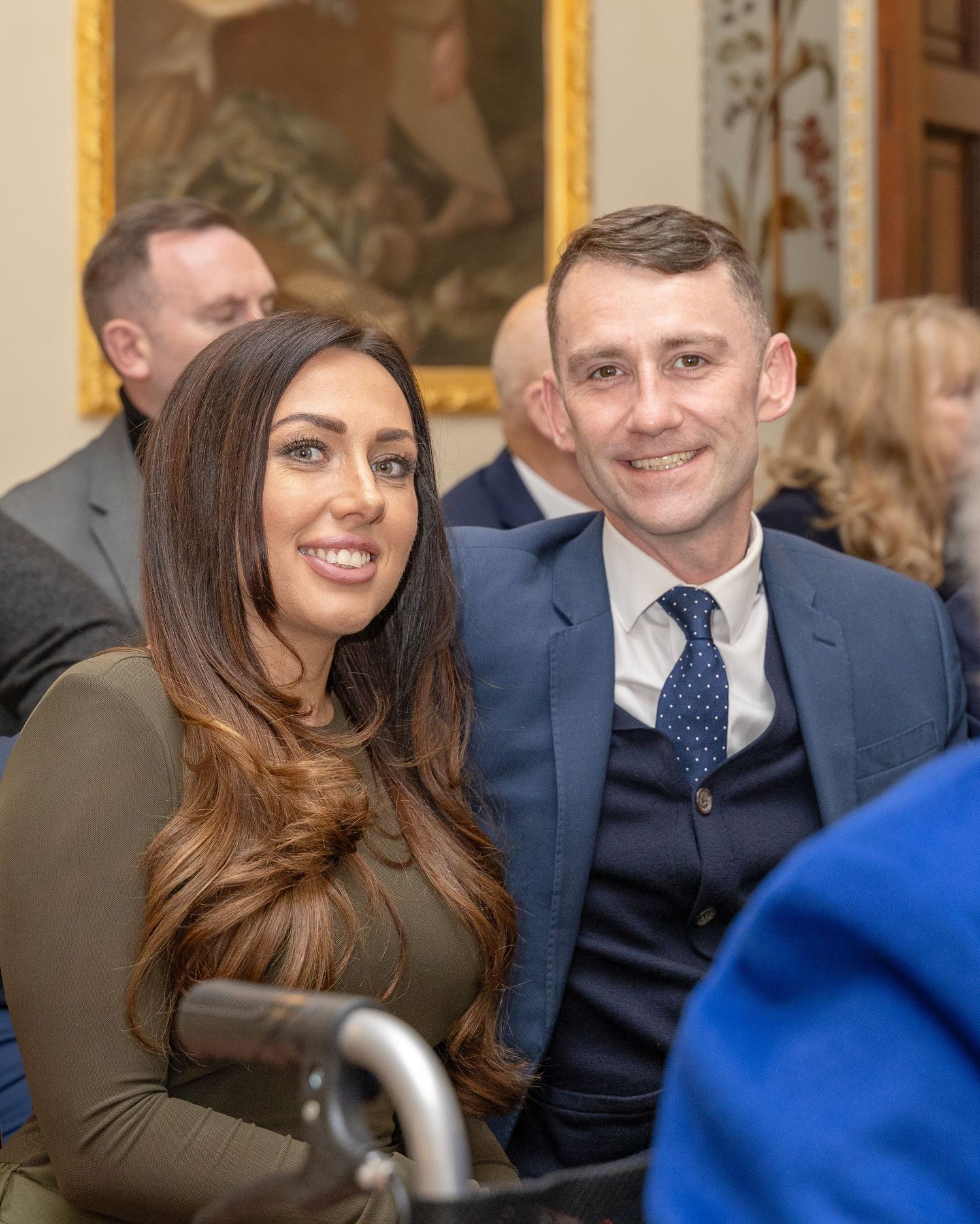 Smiling couple posing together at a formal event, woman with long brown hair and man in blue suit and tie.