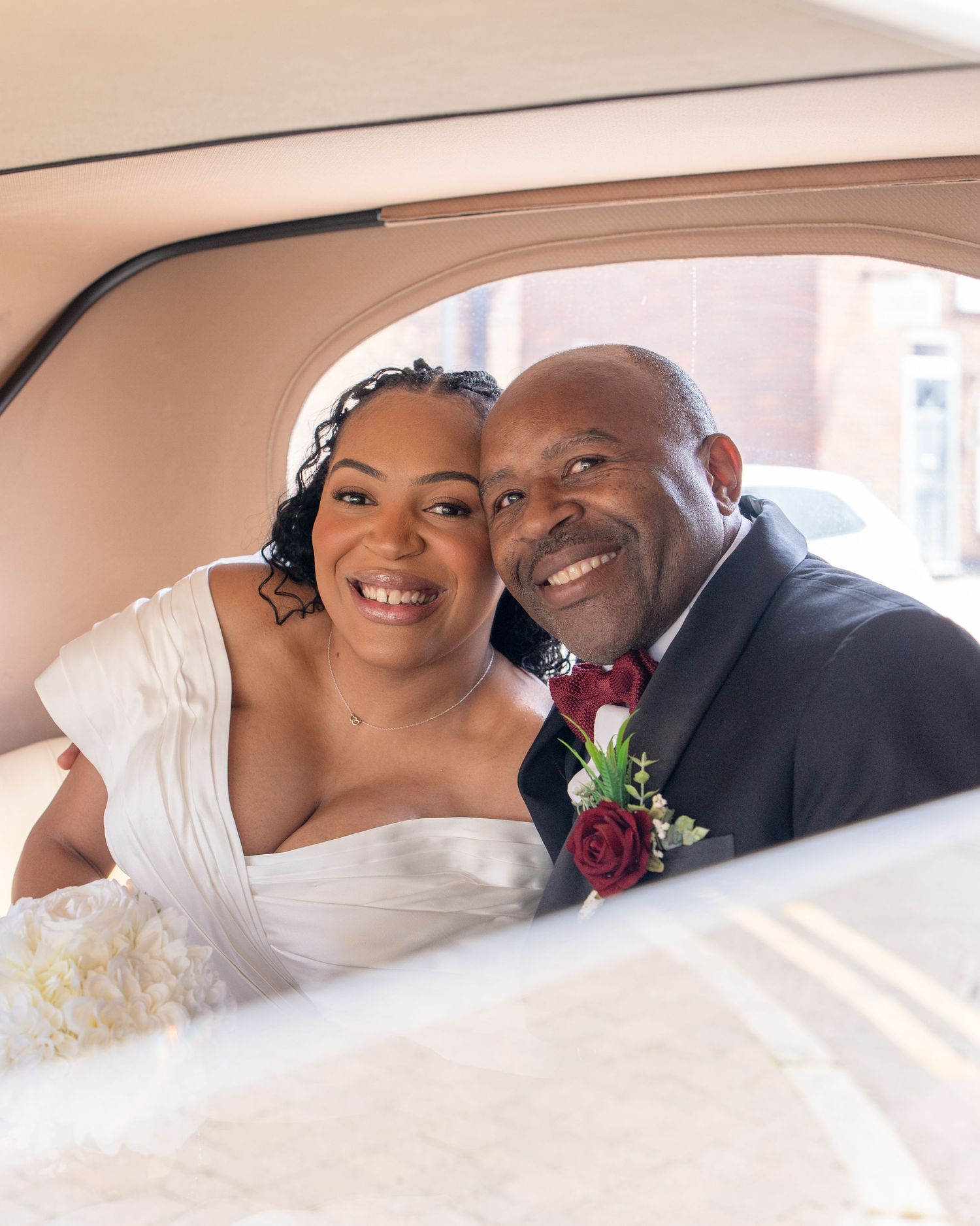 Happy bride and groom smiling together inside a vintage car on their wedding day.