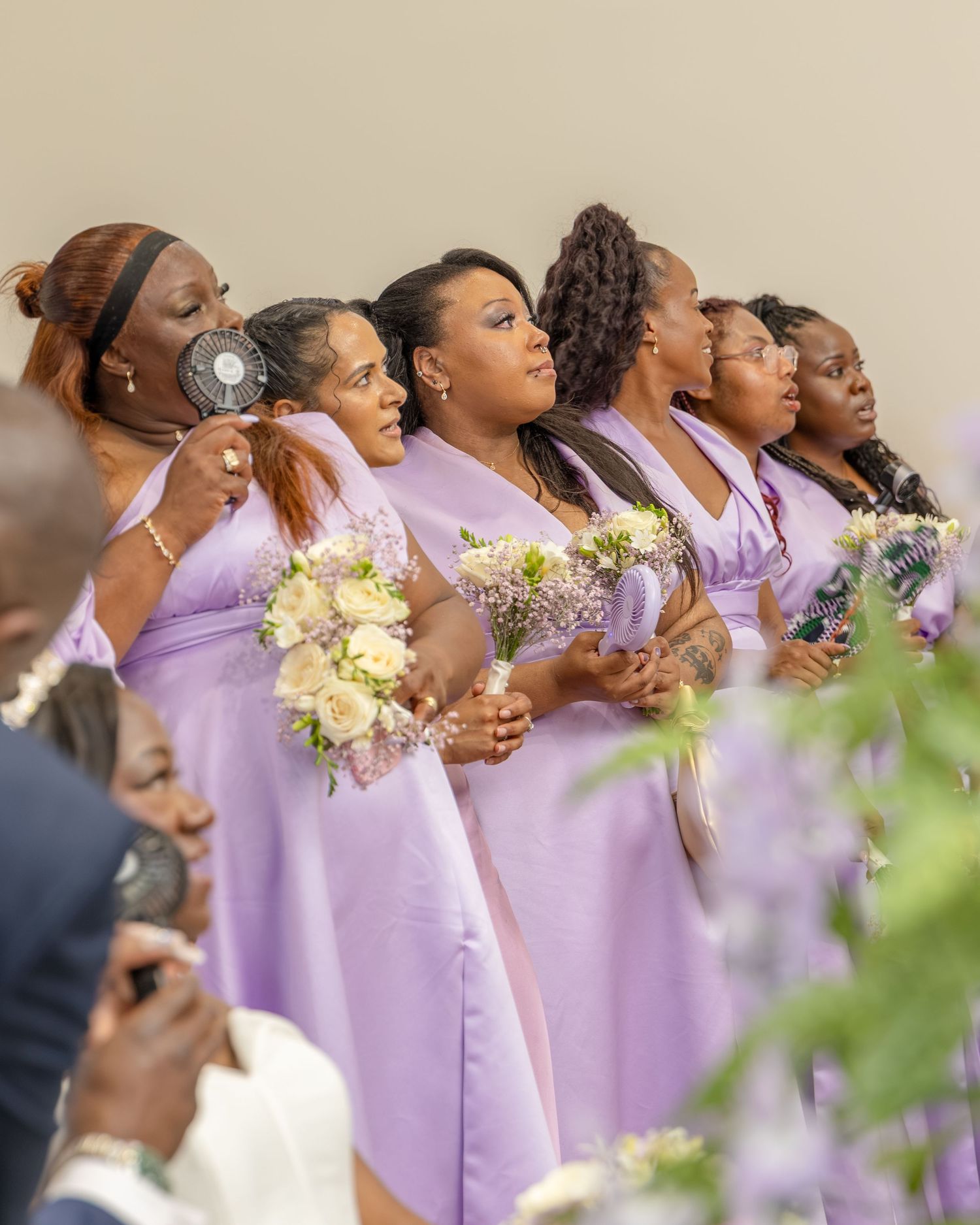 Bridesmaids in lavender dresses holding floral bouquets stand together during a wedding ceremony.