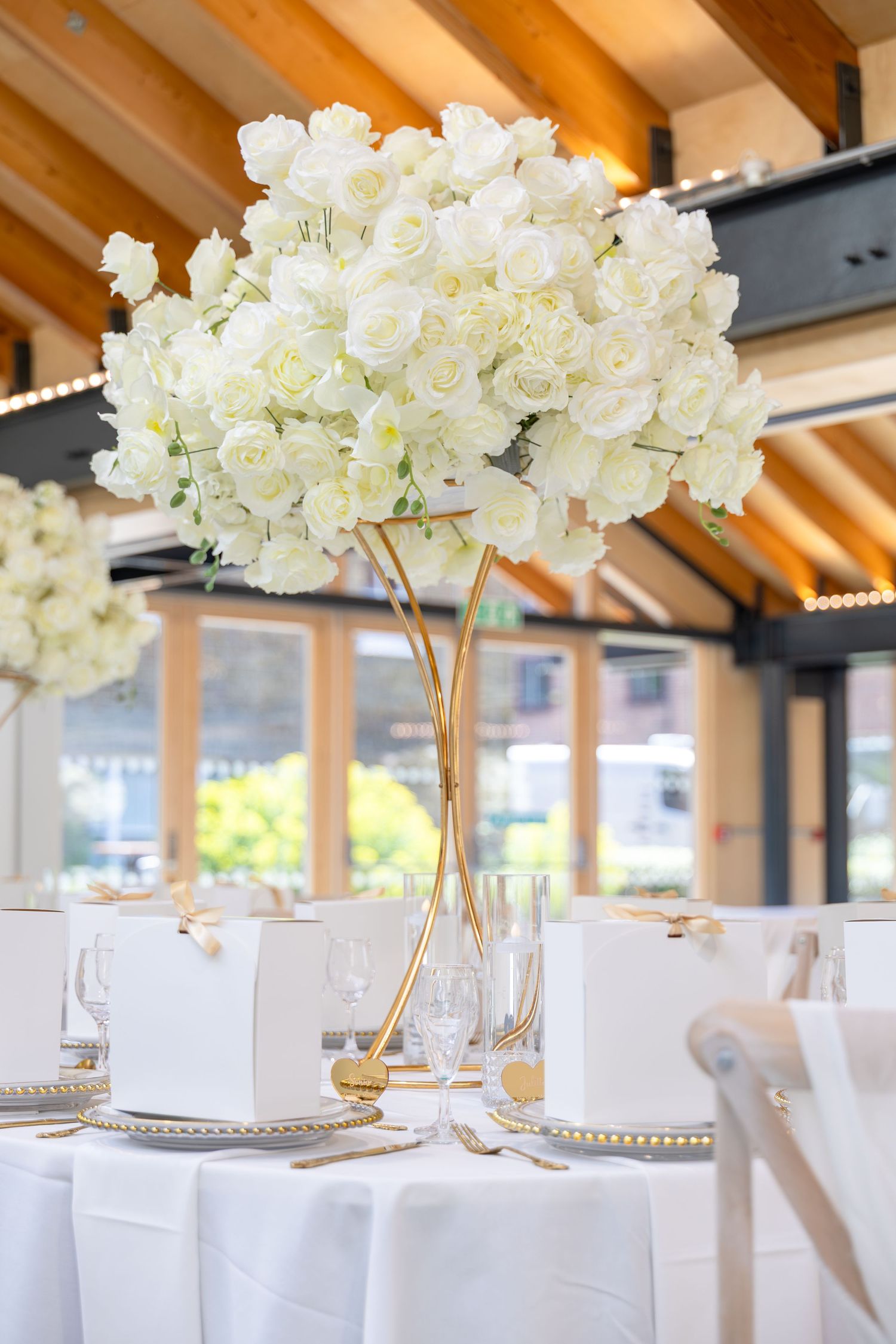 Elegant wedding reception table with tall gold vase centerpiece of white roses, white linens, and crystal glassware.