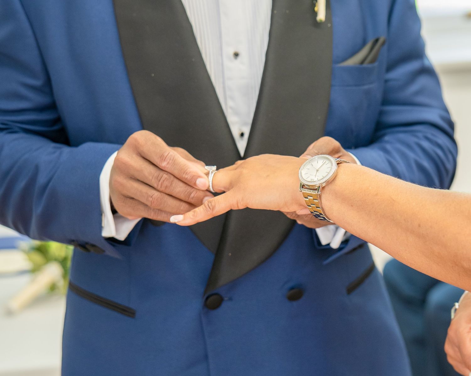 Groom in blue tuxedo placing wedding ring on bride's finger during ceremony.