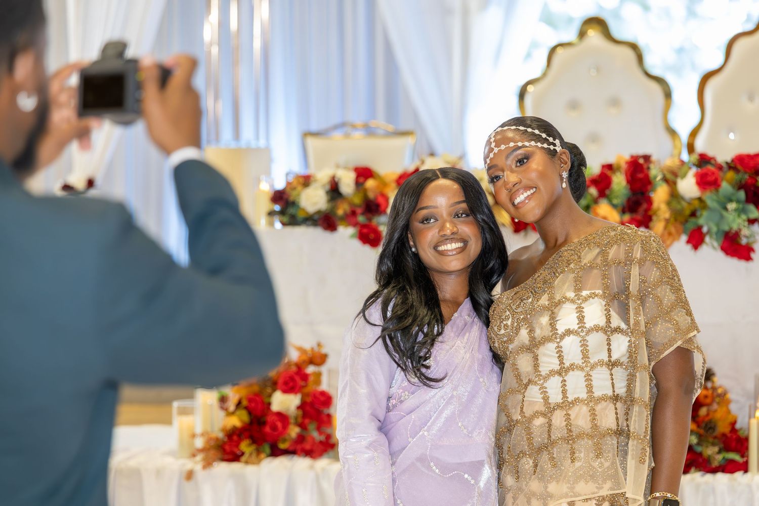Two women pose for a photo at a decorated wedding venue with floral arrangements.