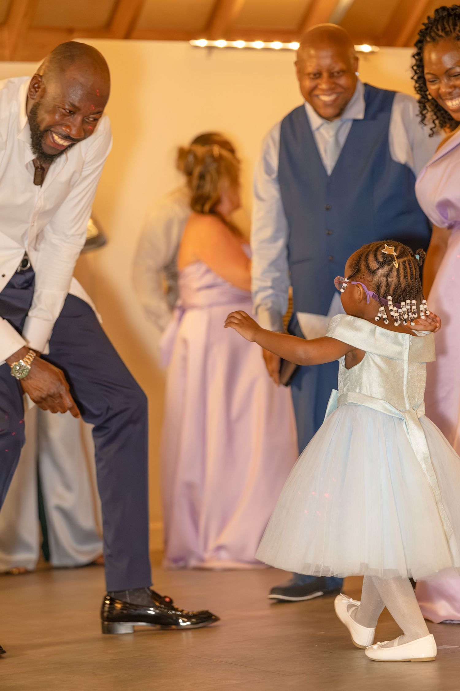 A man dances joyfully with a little girl in a white dress at a wedding reception.