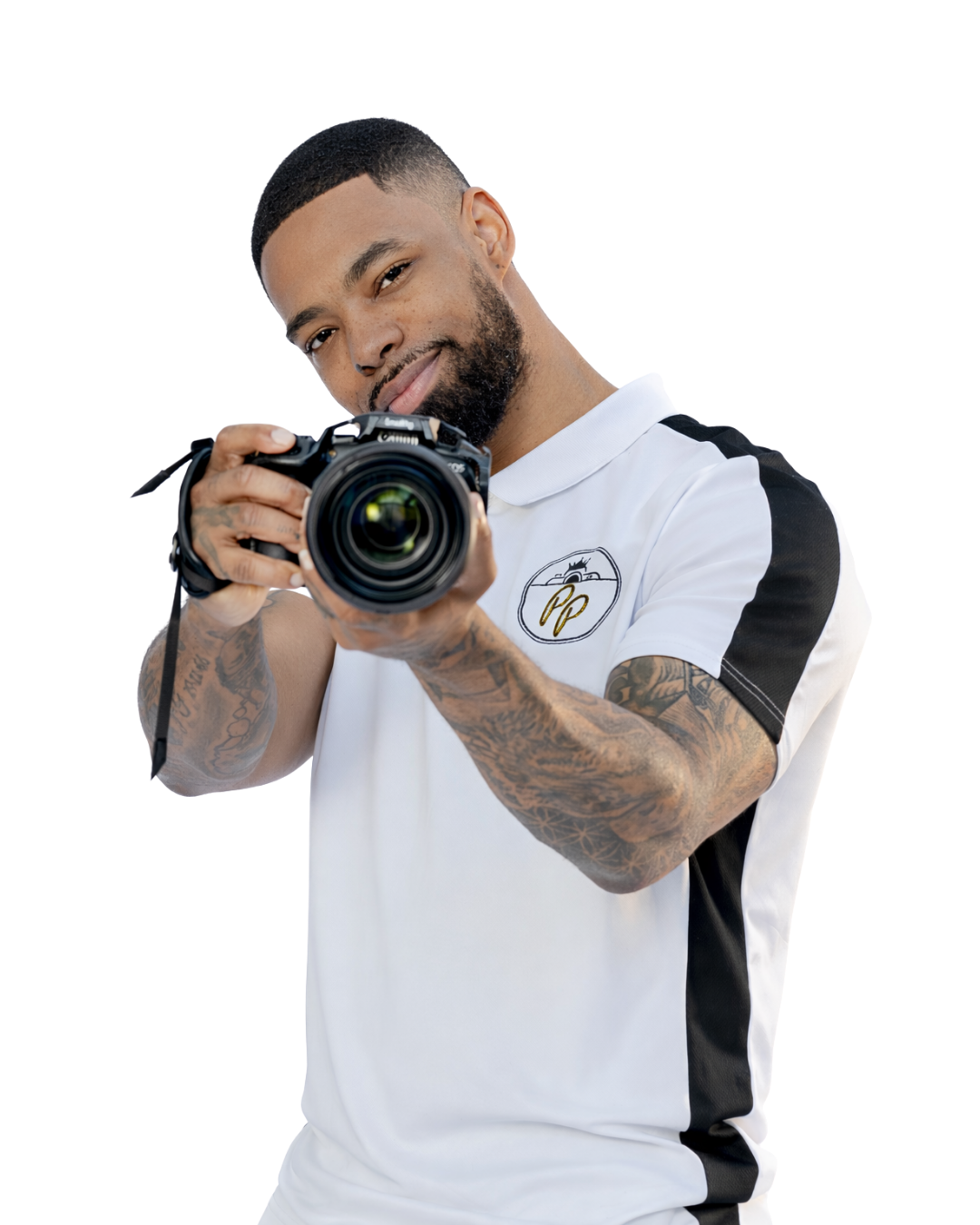 Tattooed male photographer in white shirt aiming Canon camera toward viewer on white background.