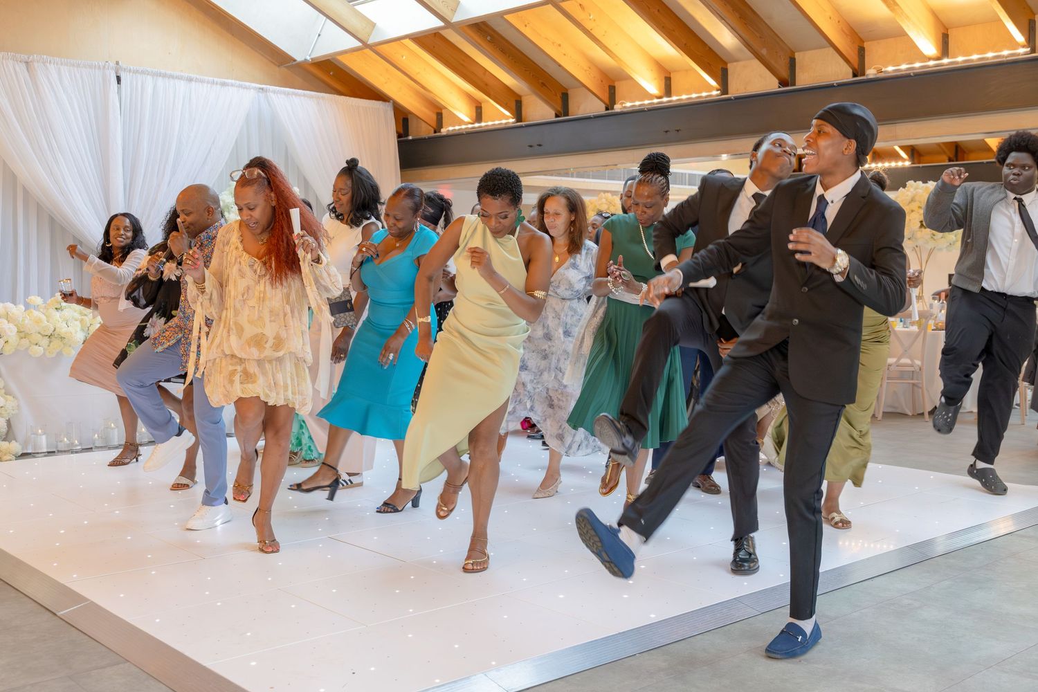 Joyful wedding guests dancing energetically on a white dance floor in an elegant decorated venue.