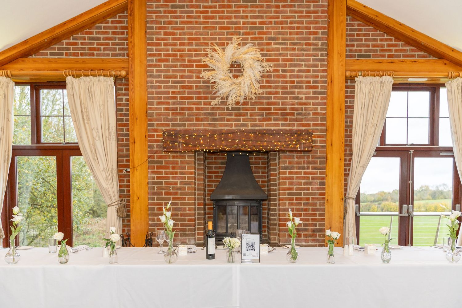 Rustic wedding venue with brick fireplace, wooden beams, and floral decorations on the head table.