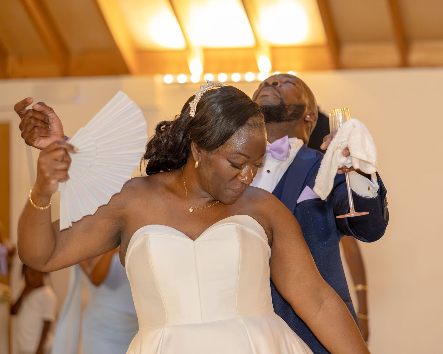 Bride in strapless white gown dancing joyfully with groom in blue suit at wedding reception.