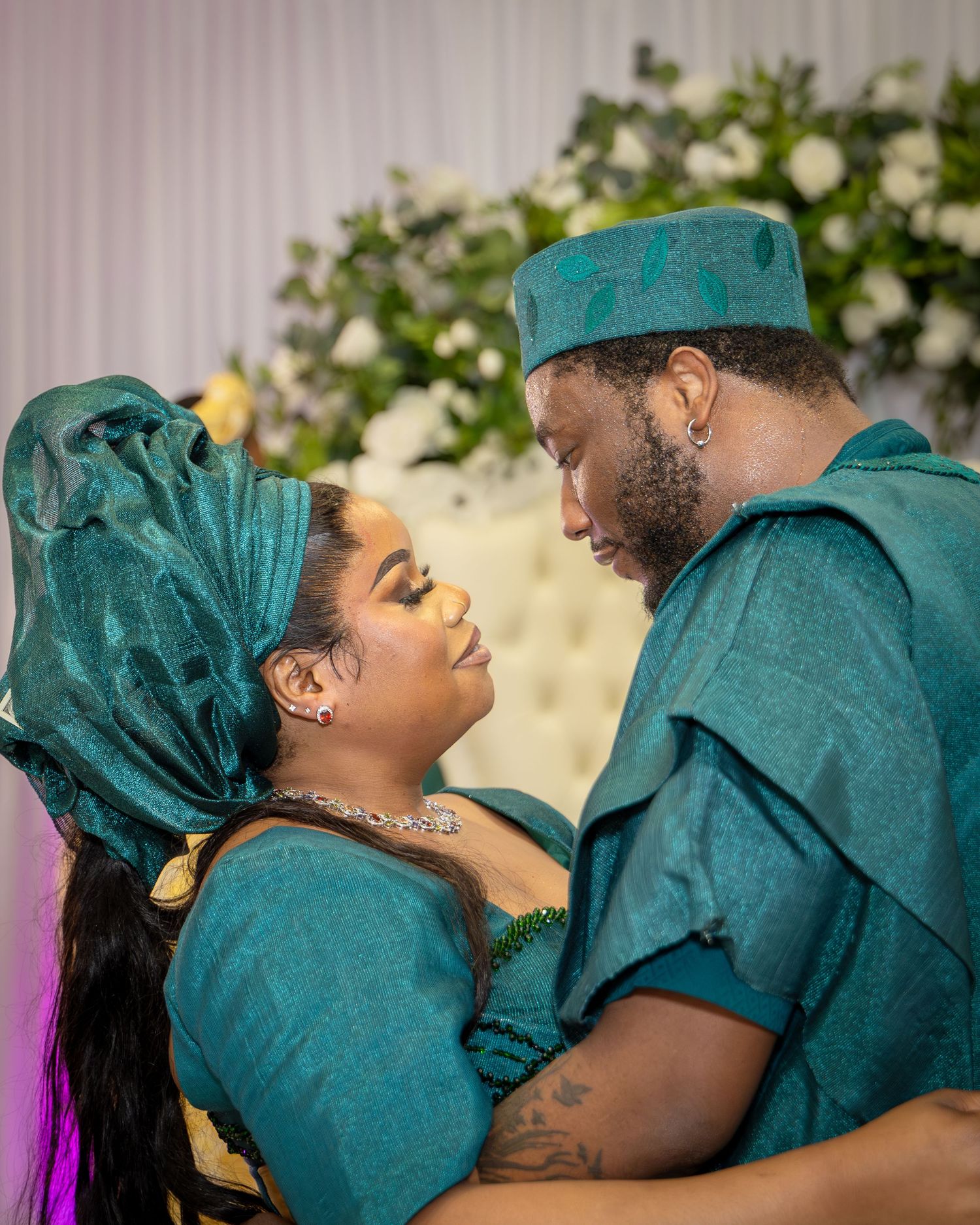 A couple in matching teal Nigerian traditional attire share a romantic moment at their traditional wedding ceremony.
