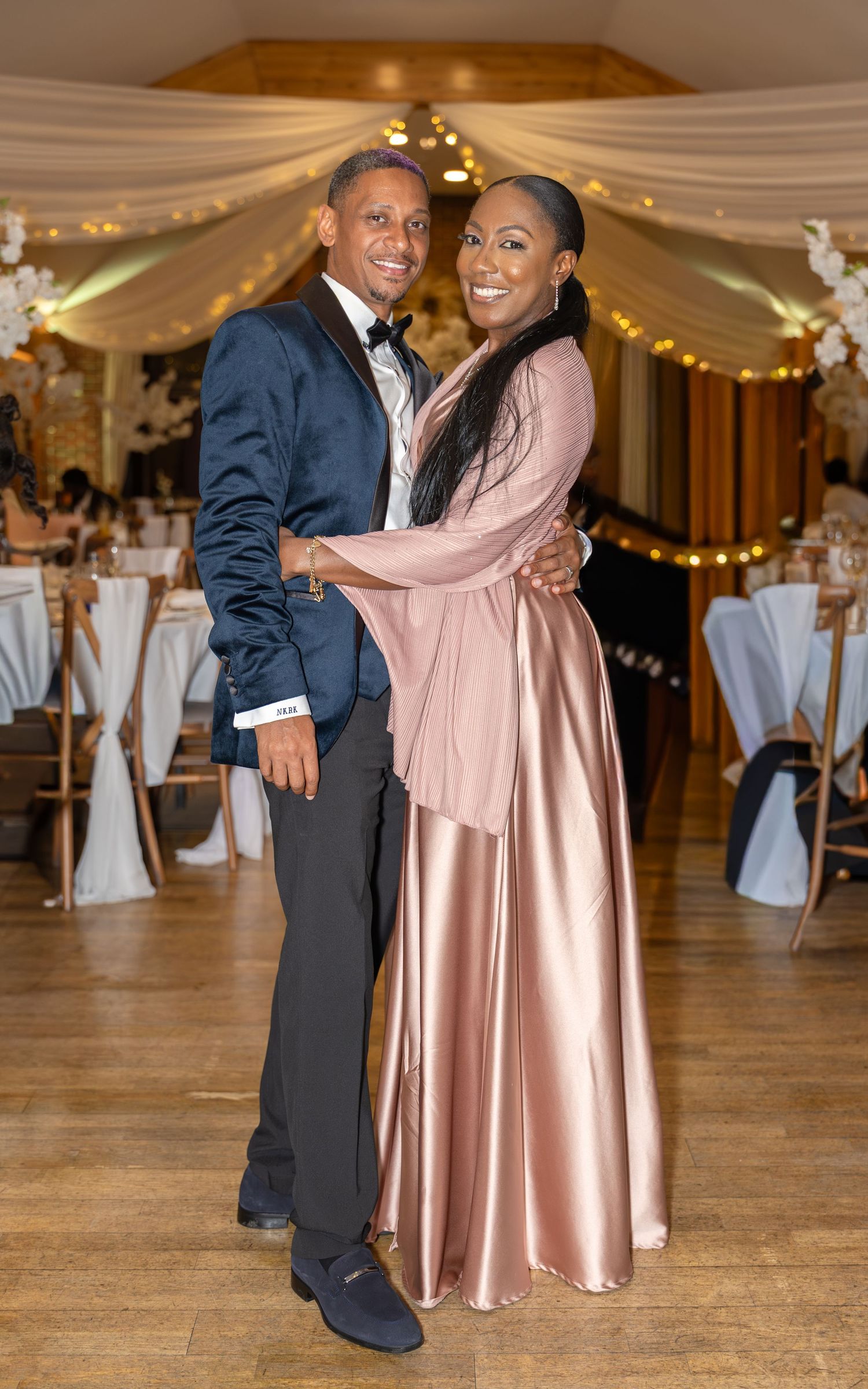 A couple shares a romantic dance embrace at a wedding reception with fairy light decor.