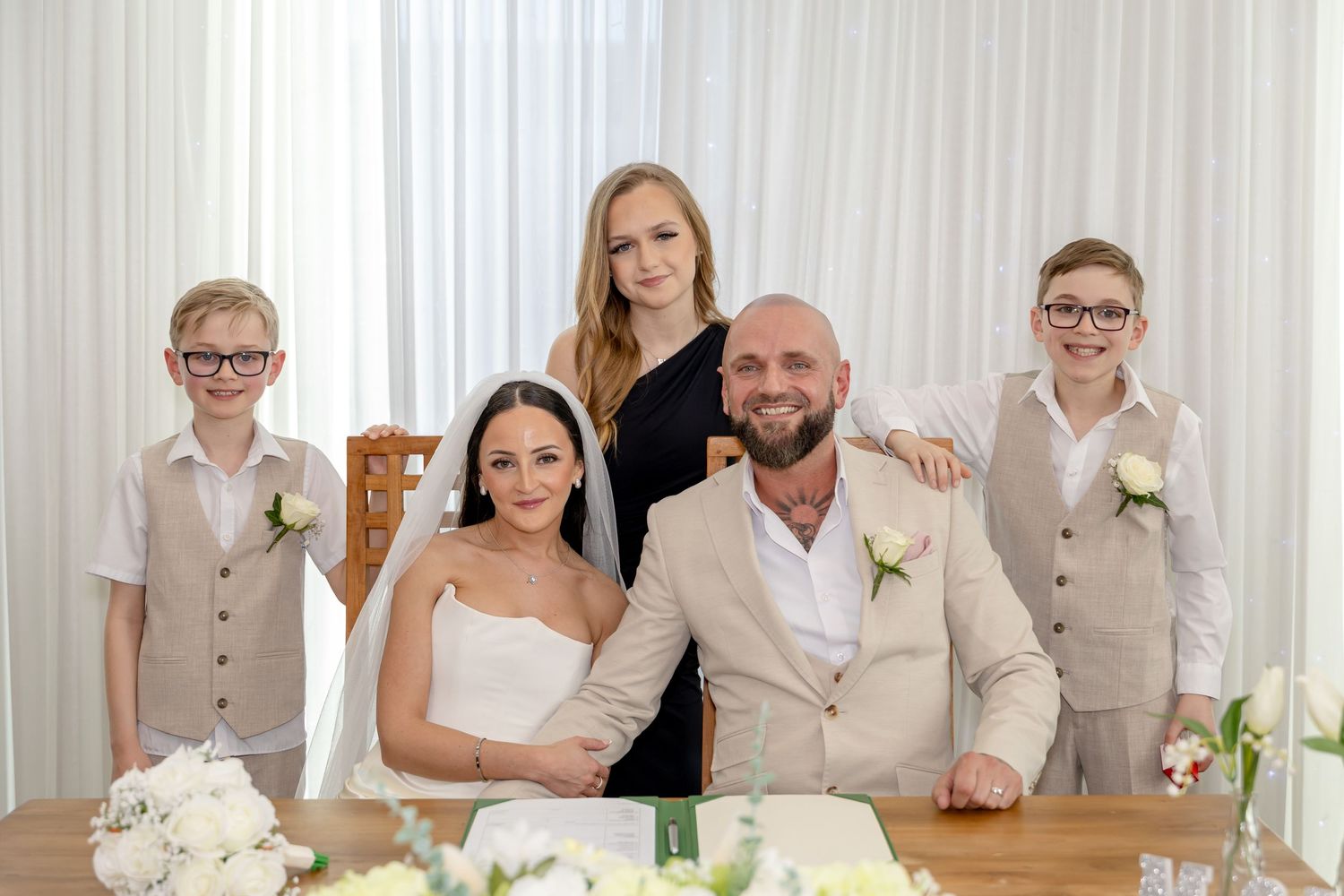 Newlyweds pose with three children at wedding signing table with white floral decor.