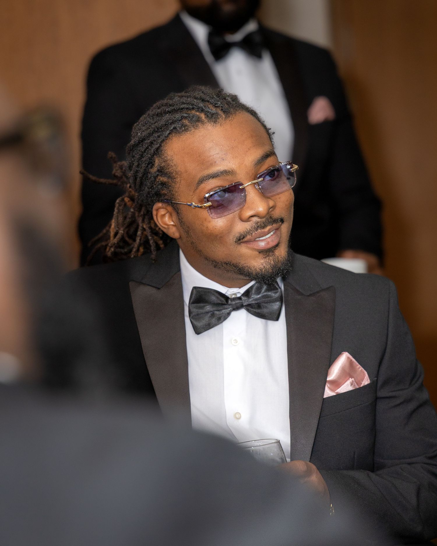 Stylish man in black tuxedo with bow tie and purple sunglasses wearing a pink pocket square.