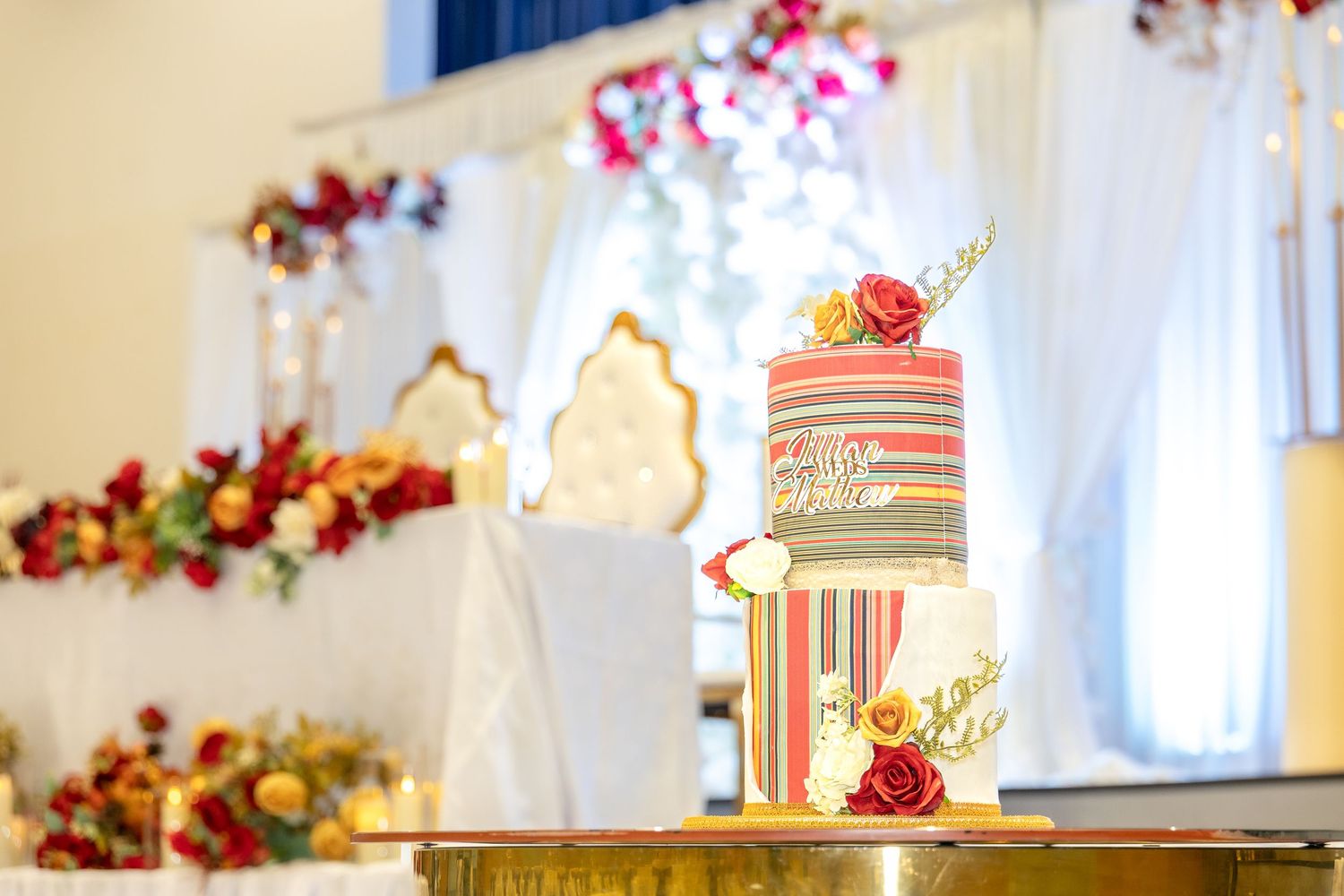 Three-tier striped wedding cake decorated with red roses on a gold stand.