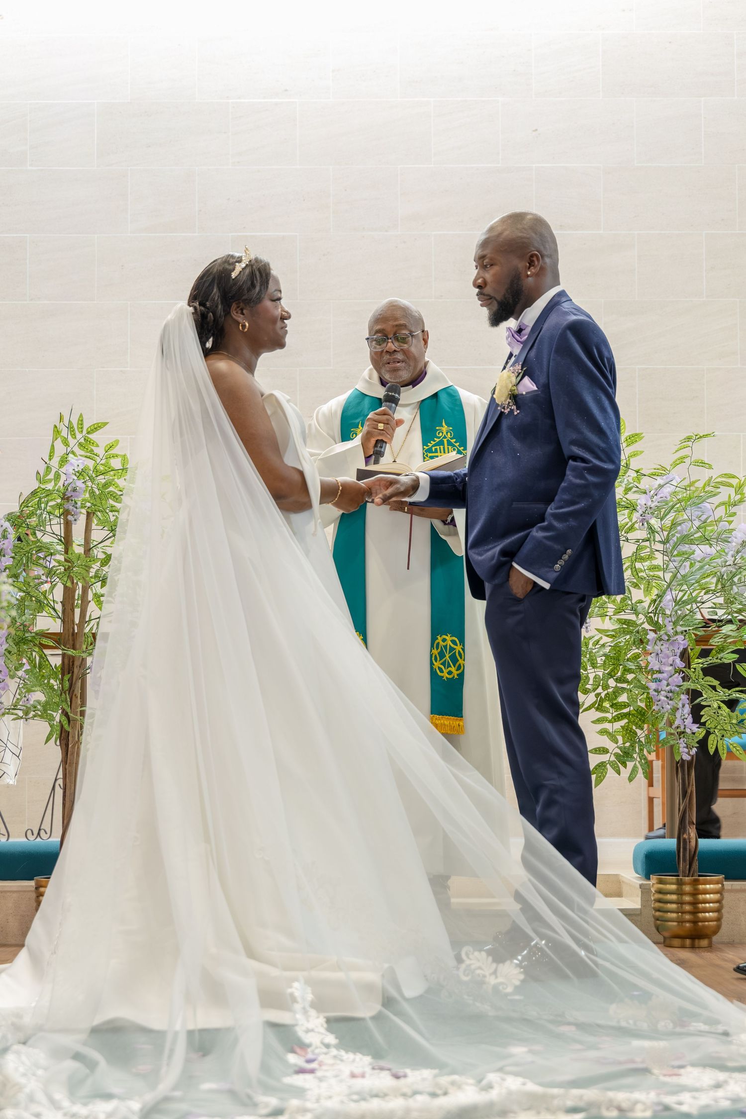 Bride and groom exchange vows at church altar with officiant in green vestments during wedding ceremony.