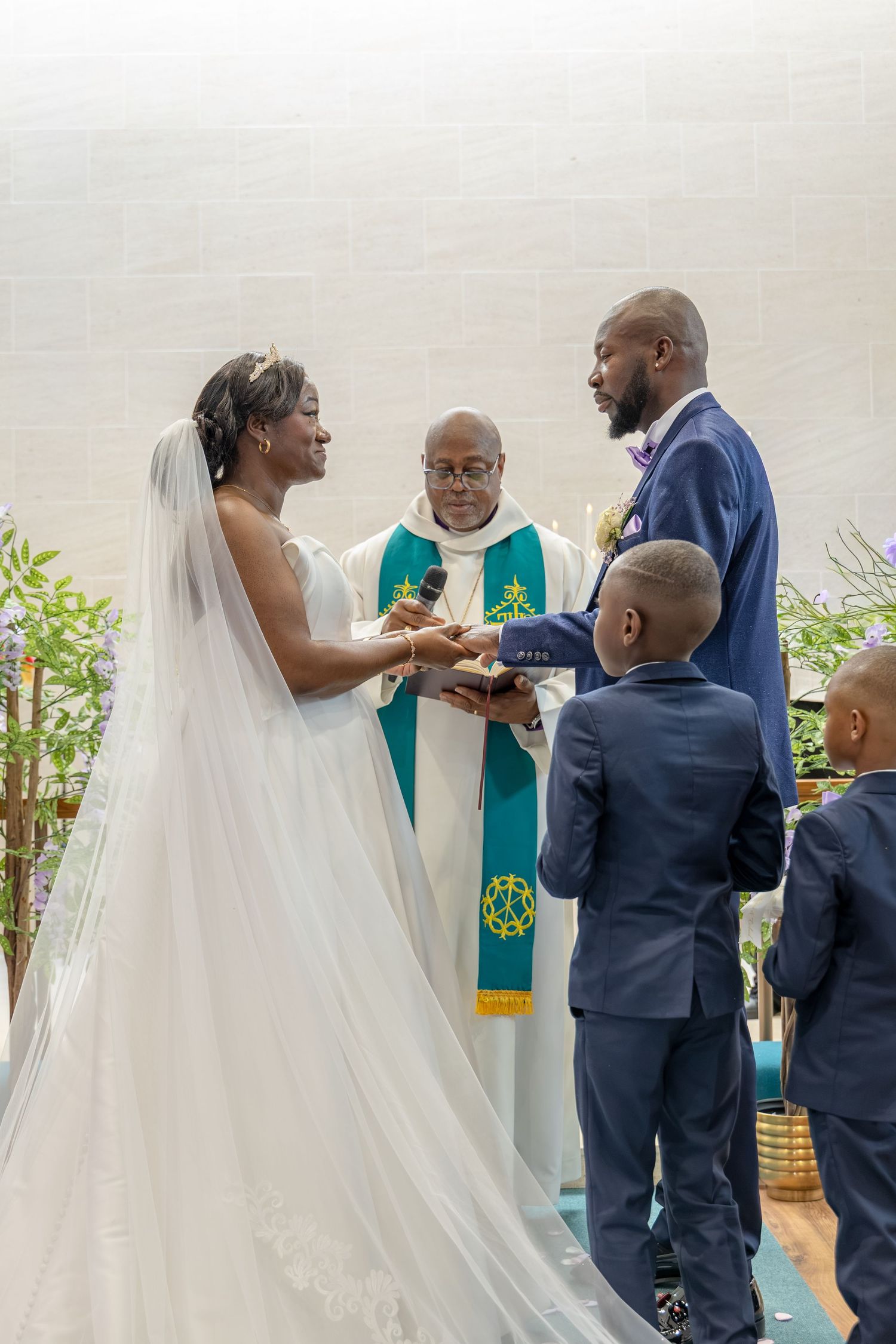 A joyful wedding ceremony with a bride and groom exchanging vows before a minister, accompanied by a young boy in a navy suit.