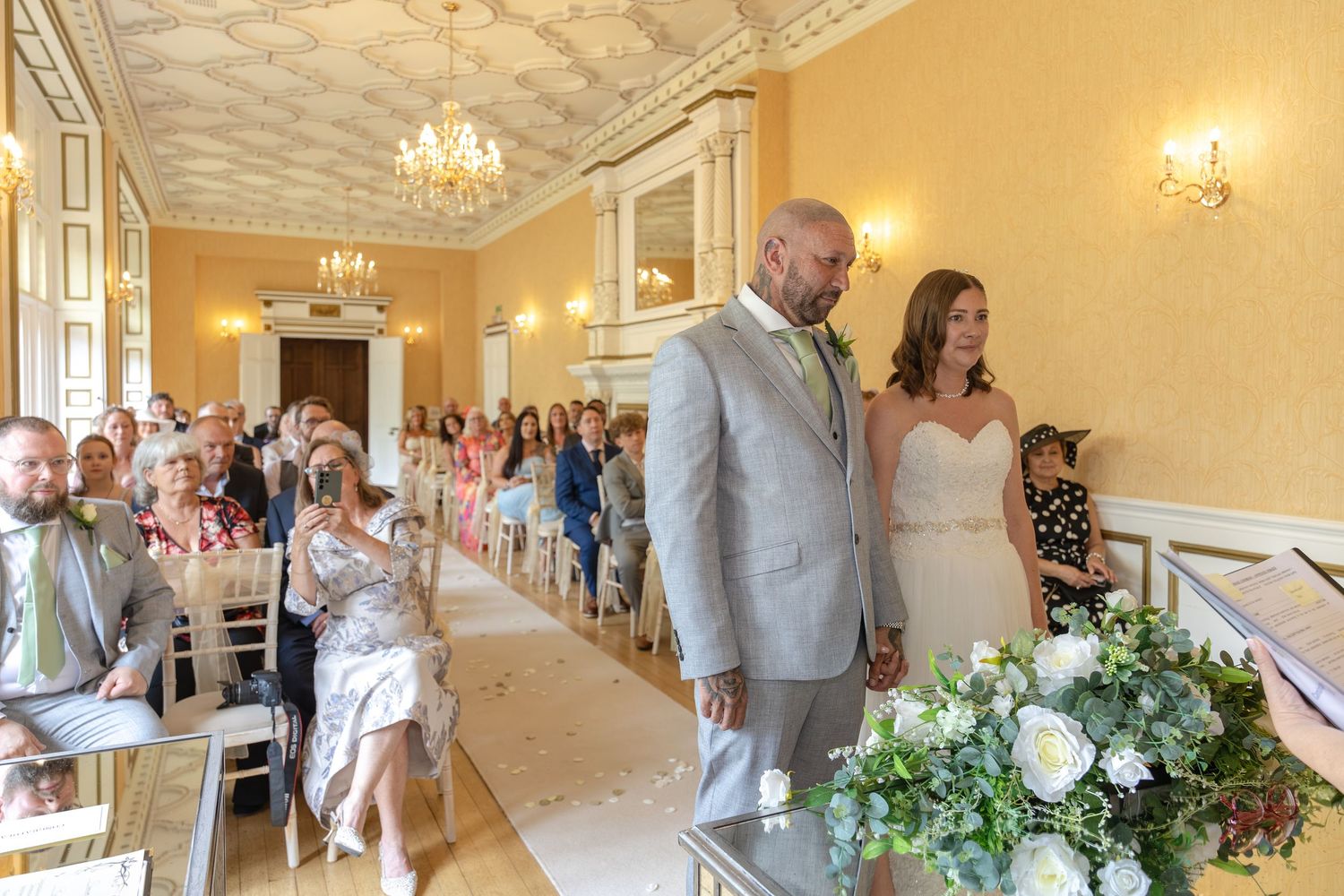 Bride and groom stand at the altar in an elegant ballroom venue during their wedding ceremony with seated guests.