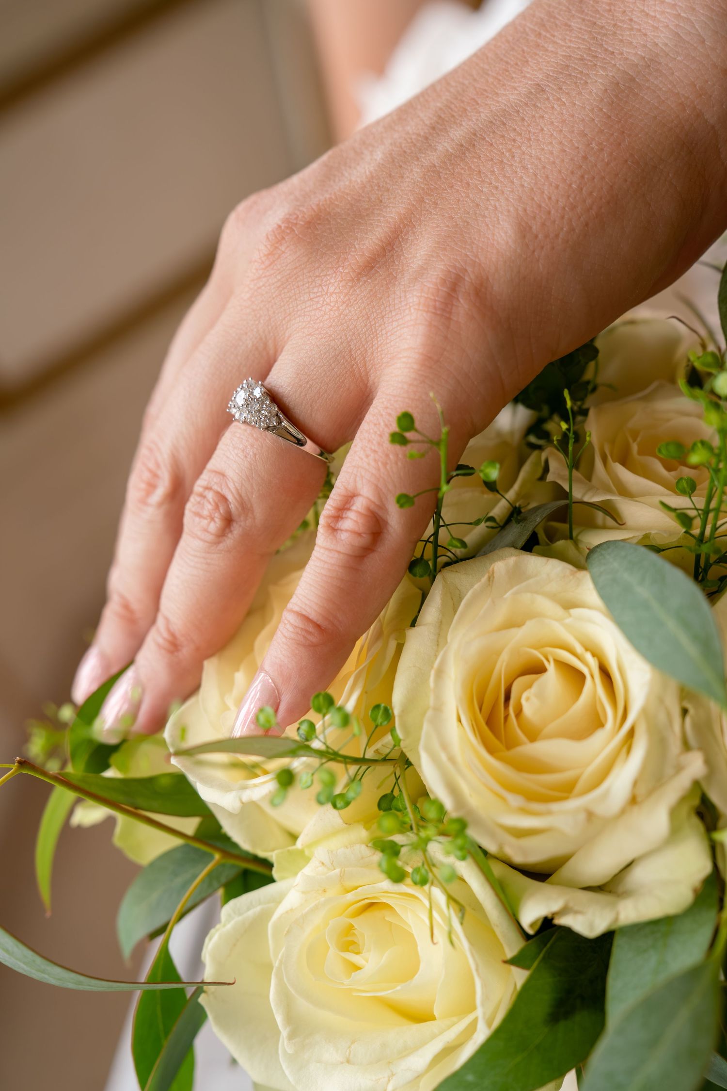 Bride's hand with diamond engagement ring resting on a bouquet of cream roses and greenery.