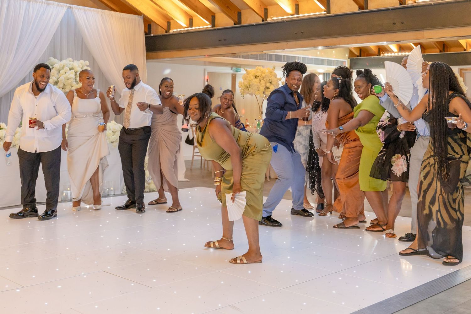 Guests dancing and celebrating at a wedding reception on a white dance floor in an elegant venue.