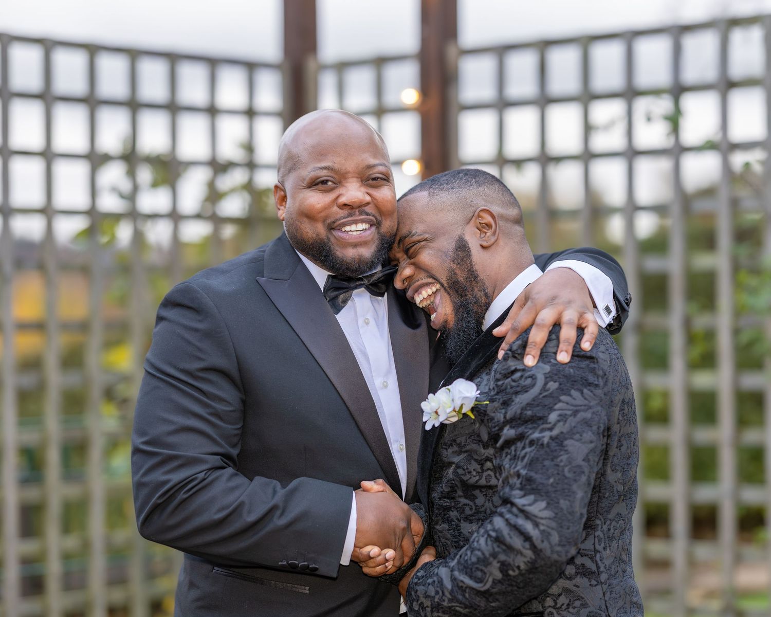 Two grooms share a joyful embrace outdoors during their wedding celebration.