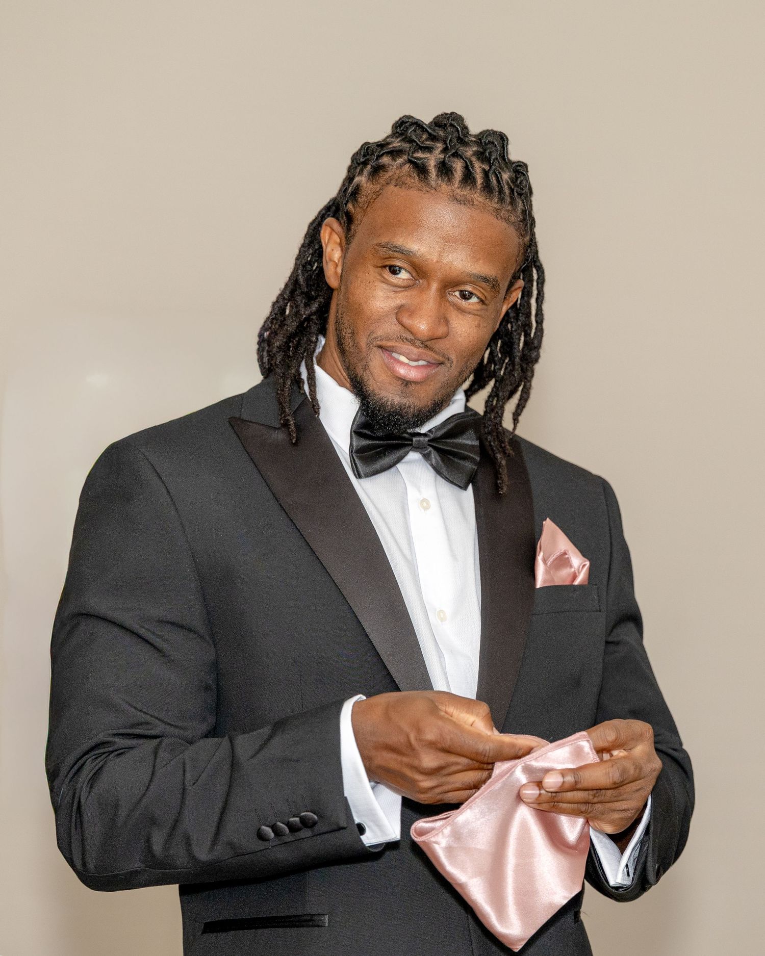 Elegant man in black tuxedo with bow tie holding a pink pocket square at a formal occasion.
