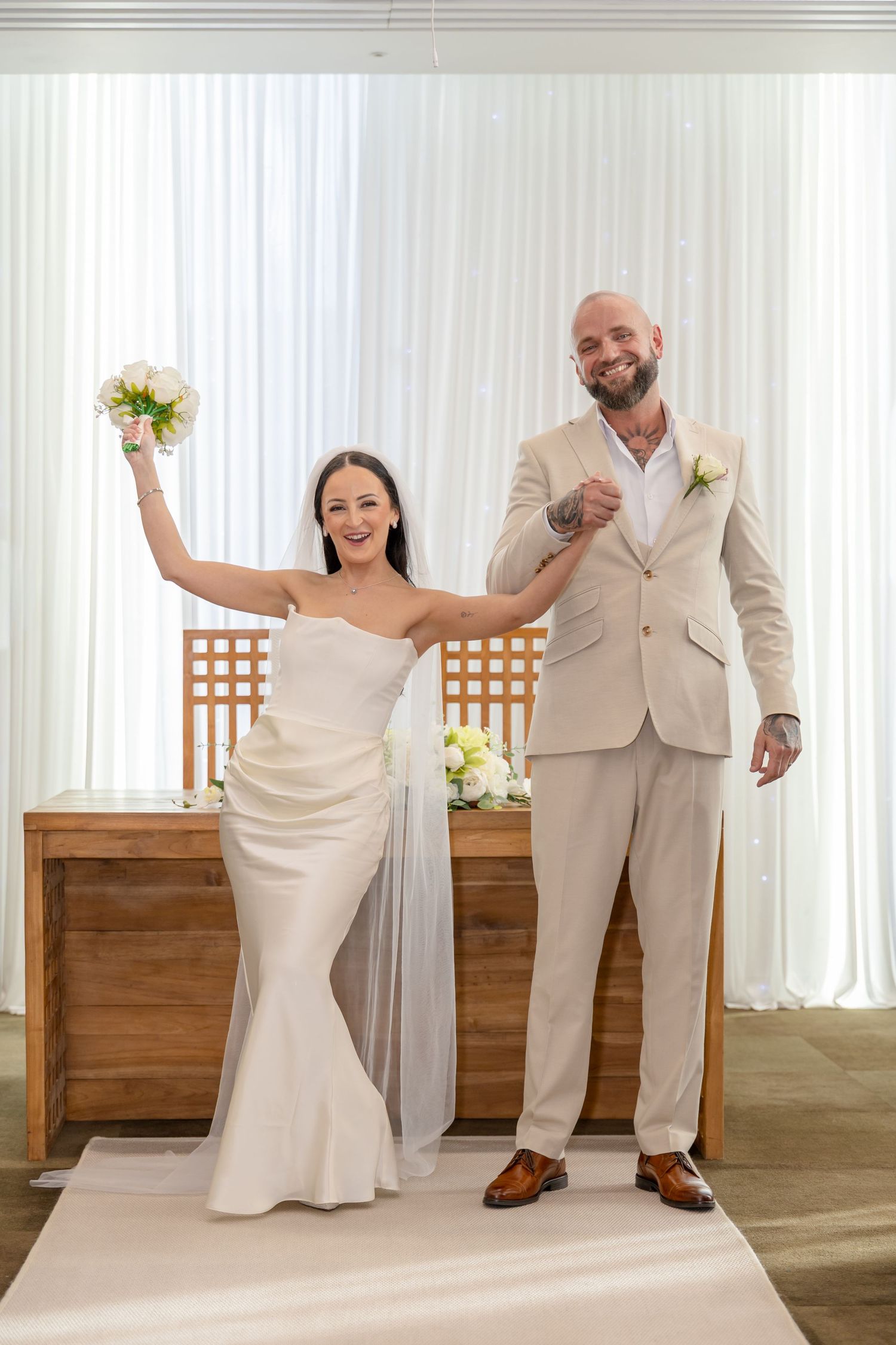 Joyful bride raises bouquet in celebration as groom smiles beside her at wedding ceremony altar.