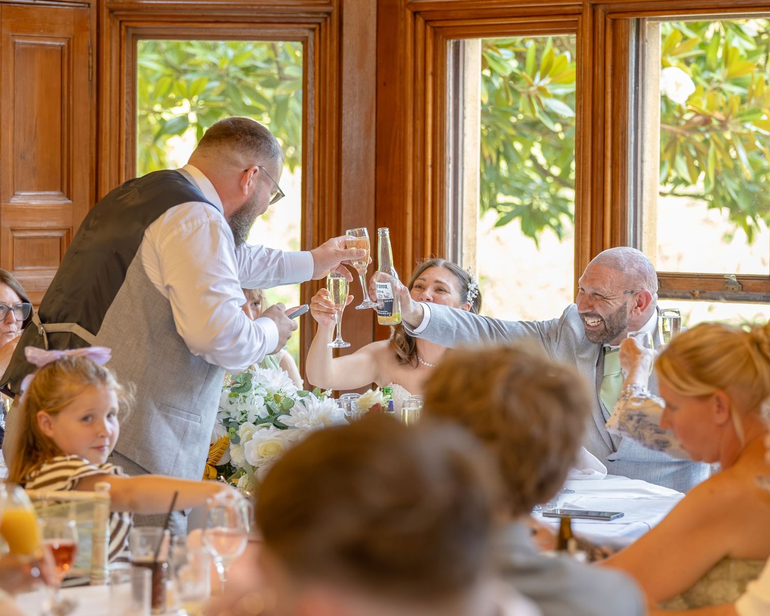 Wedding guests raising champagne glasses in a toast at an elegant wood-paneled reception venue.
