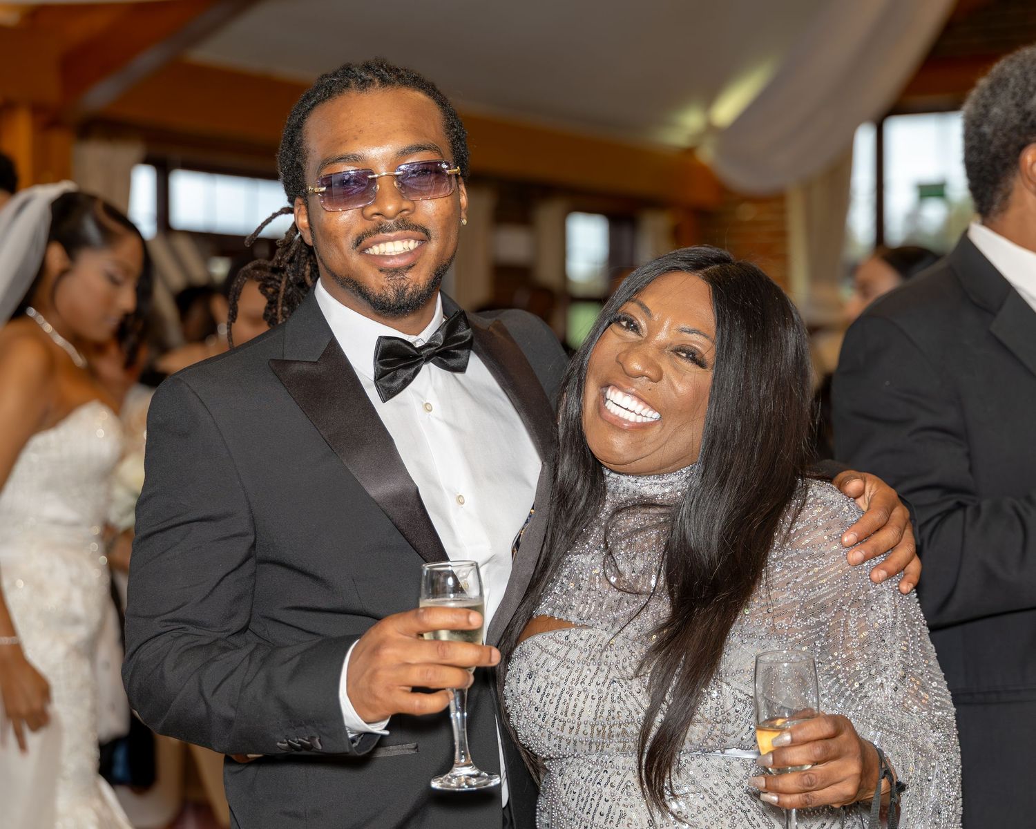 Man in tuxedo and woman in silver dress smiling together at wedding celebration.