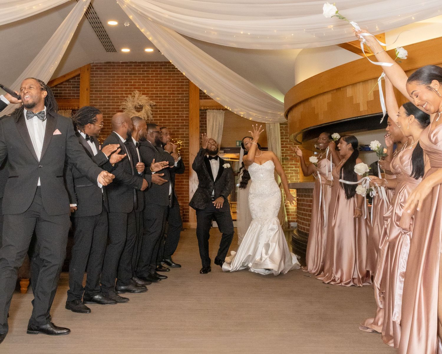 Wedding party celebrates as bride and groom make grand entrance through cheering groomsmen and bridesmaids.
