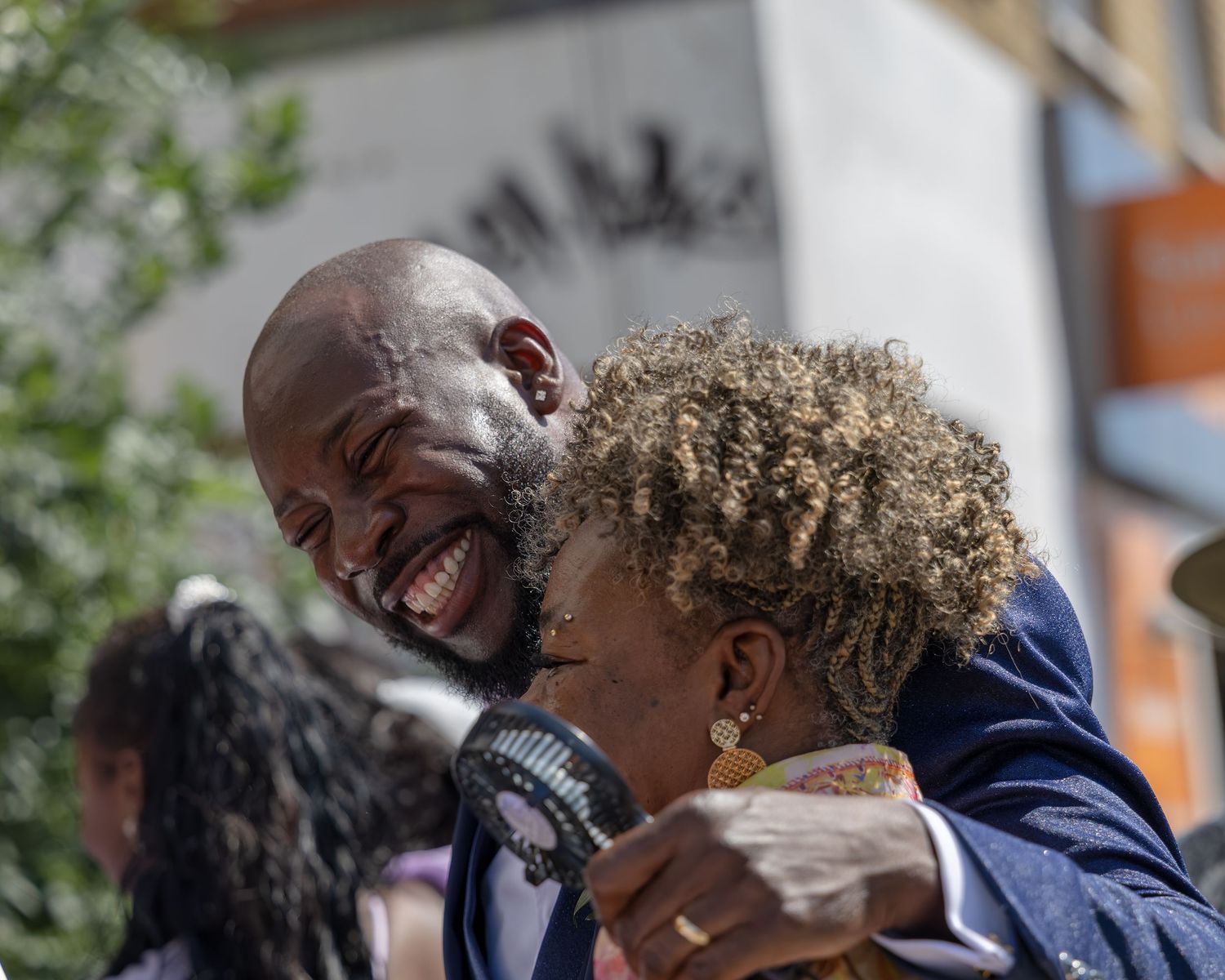 Two people sharing a warm embrace and joyful laughter outdoors on a sunny day.