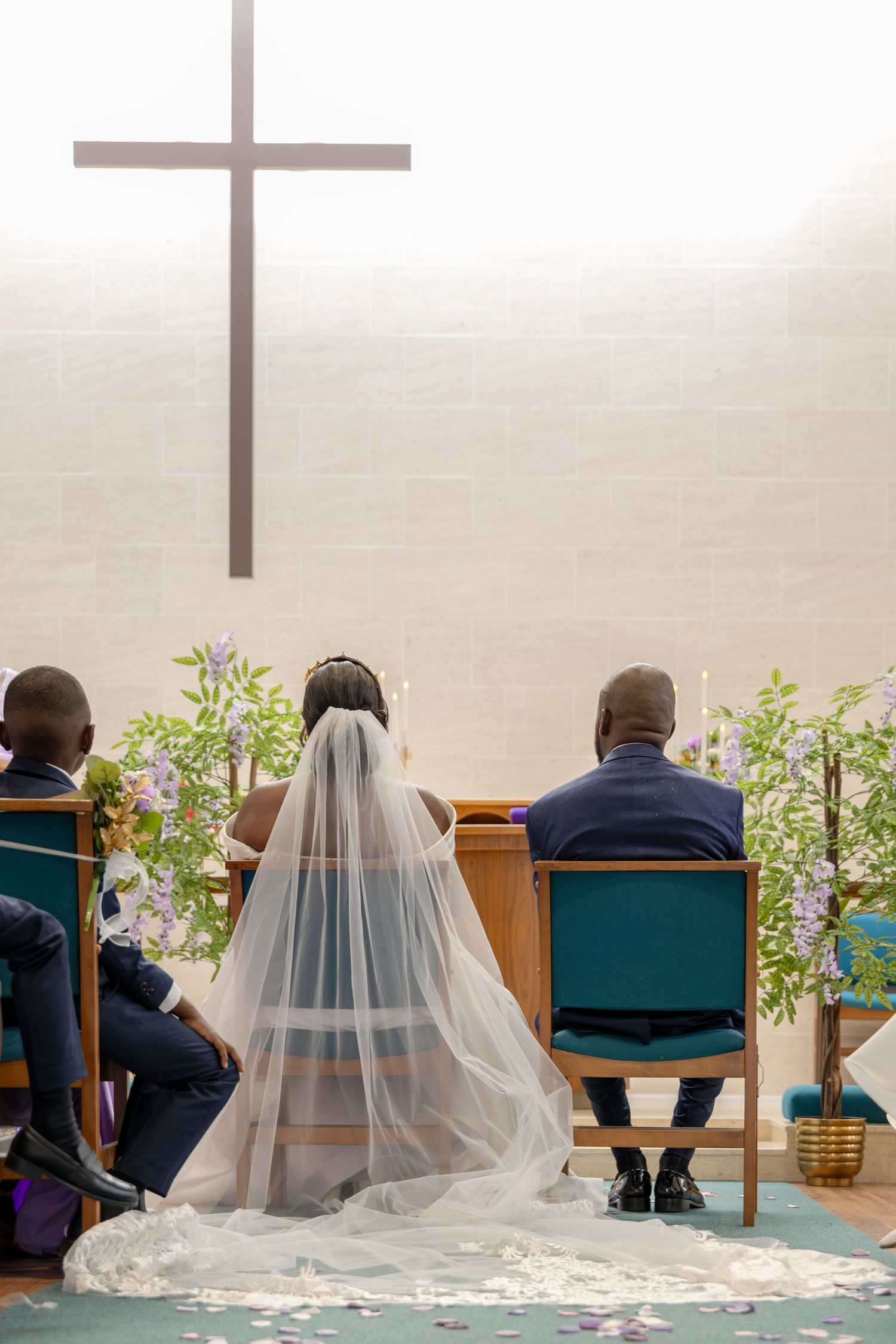 Bride and groom seated at church altar with cross, bride wearing white veil, during wedding ceremony.