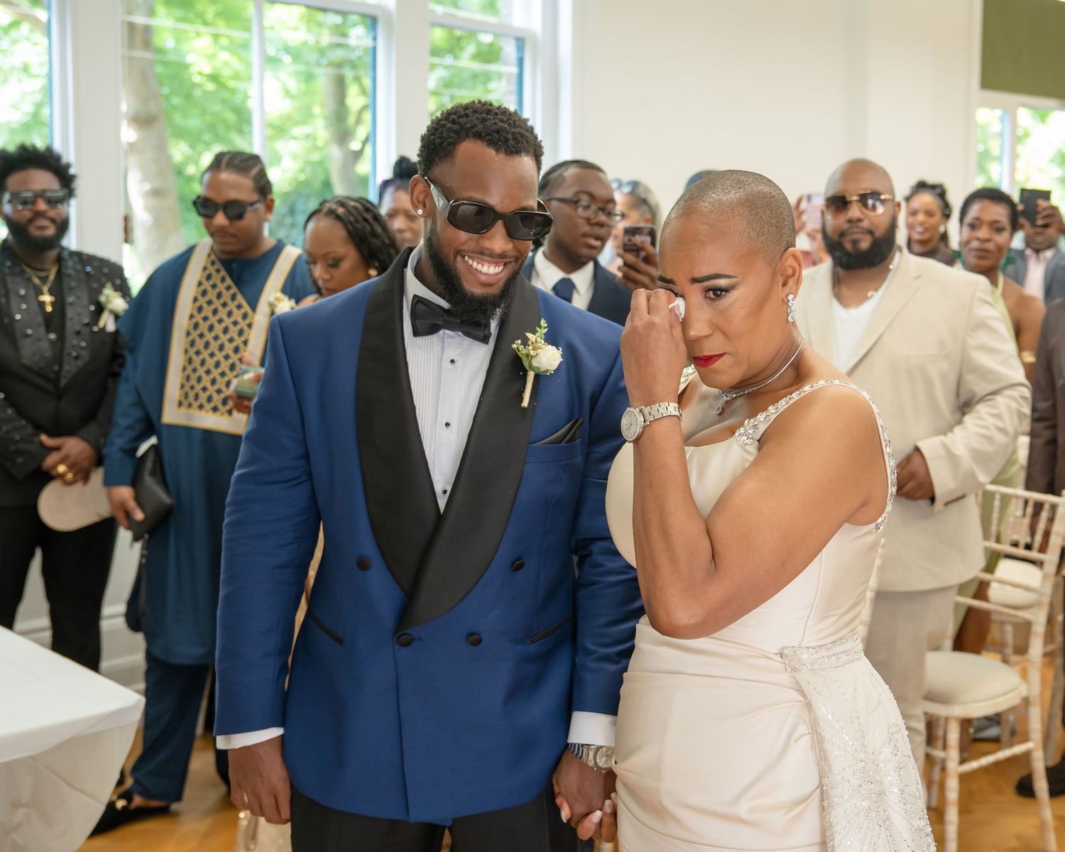 Couple in wedding attire, groom in blue tuxedo and bride in white gown, sharing emotional moment at ceremony.