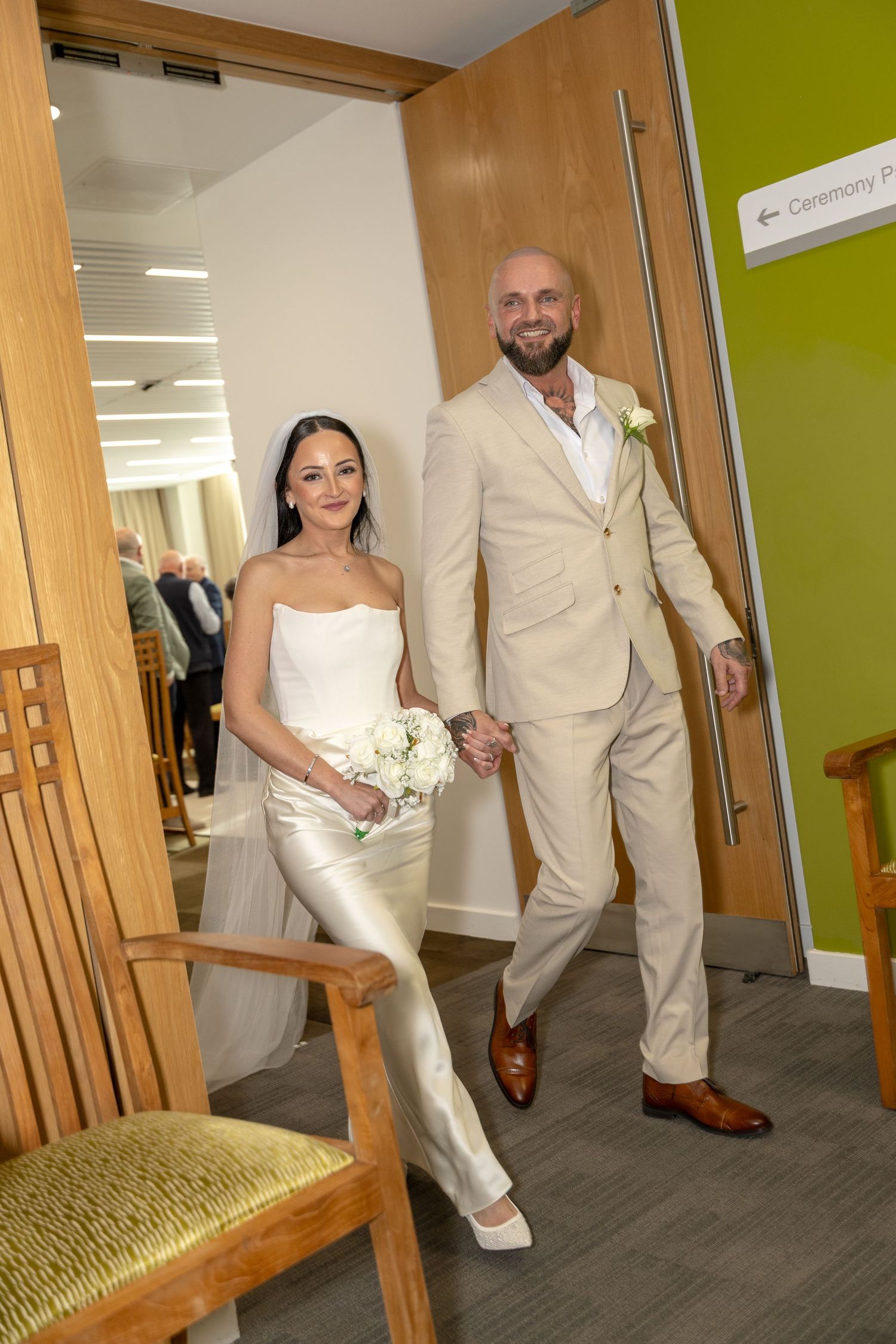 Bride and groom enter the ceremony room at Hertfordshire Register Office holding hands and smiling.