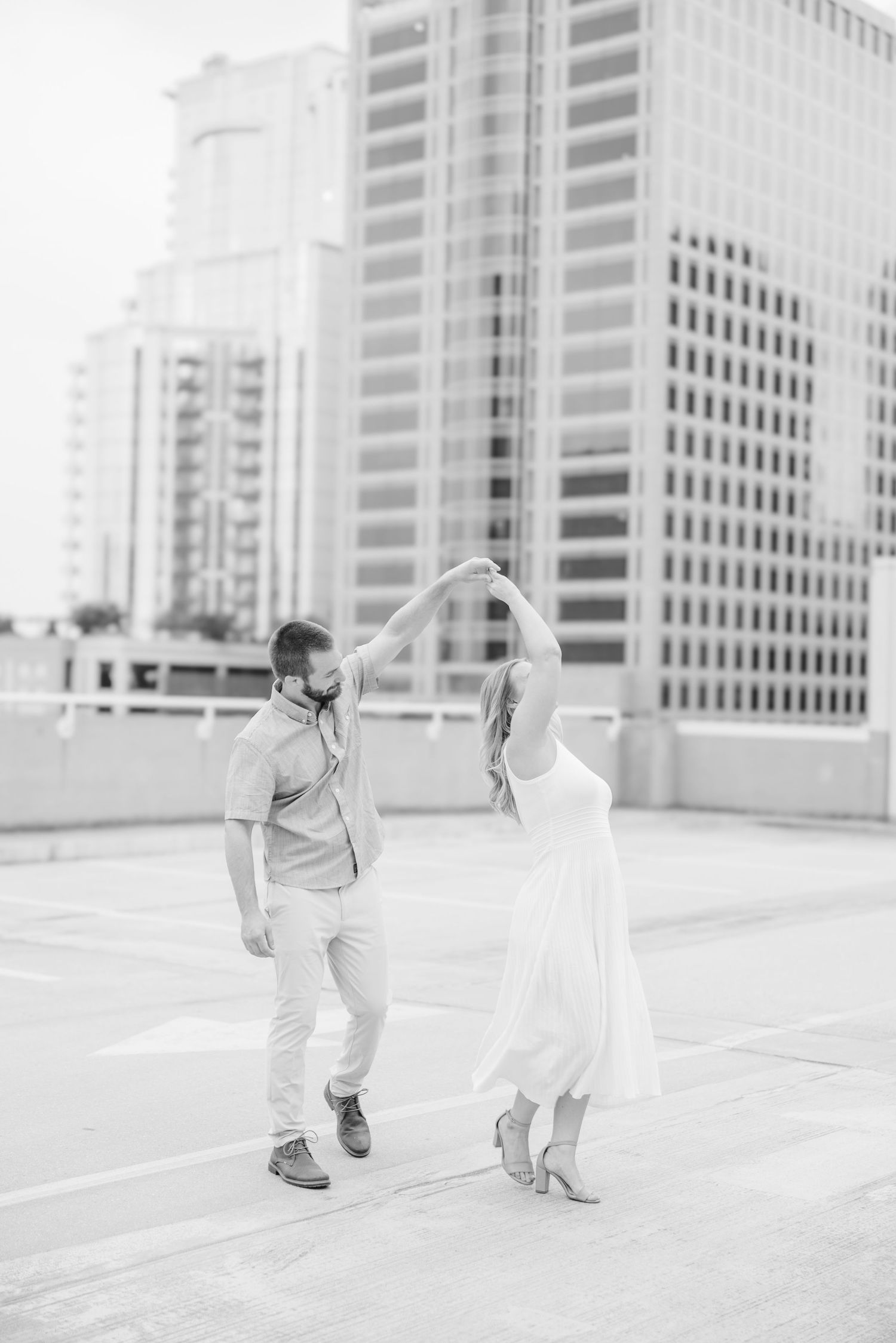 Playful couple runs and dances together on urban rooftop parking deck.