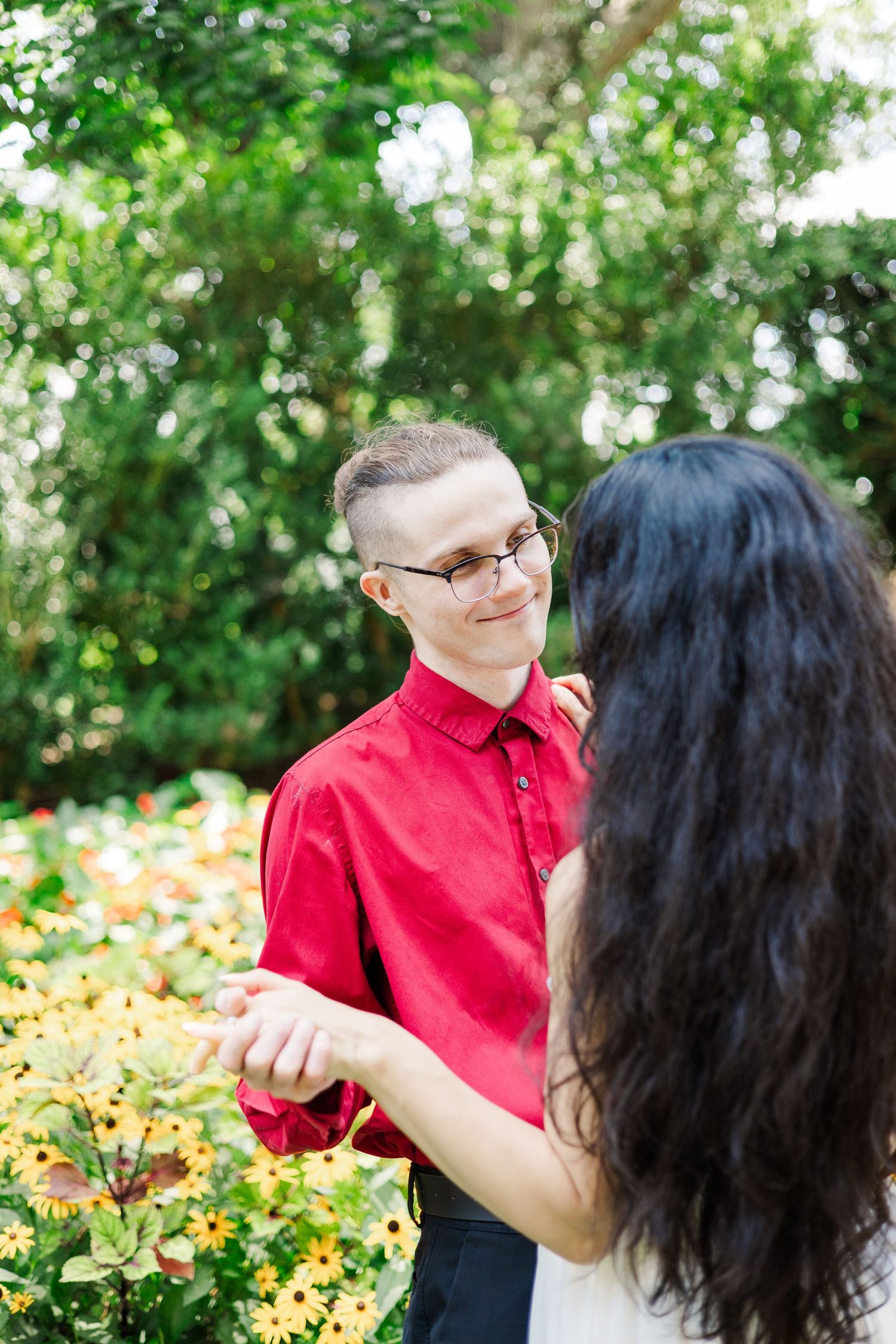 A couple shares playful moments in a garden setting with blooming flowers and green foliage.