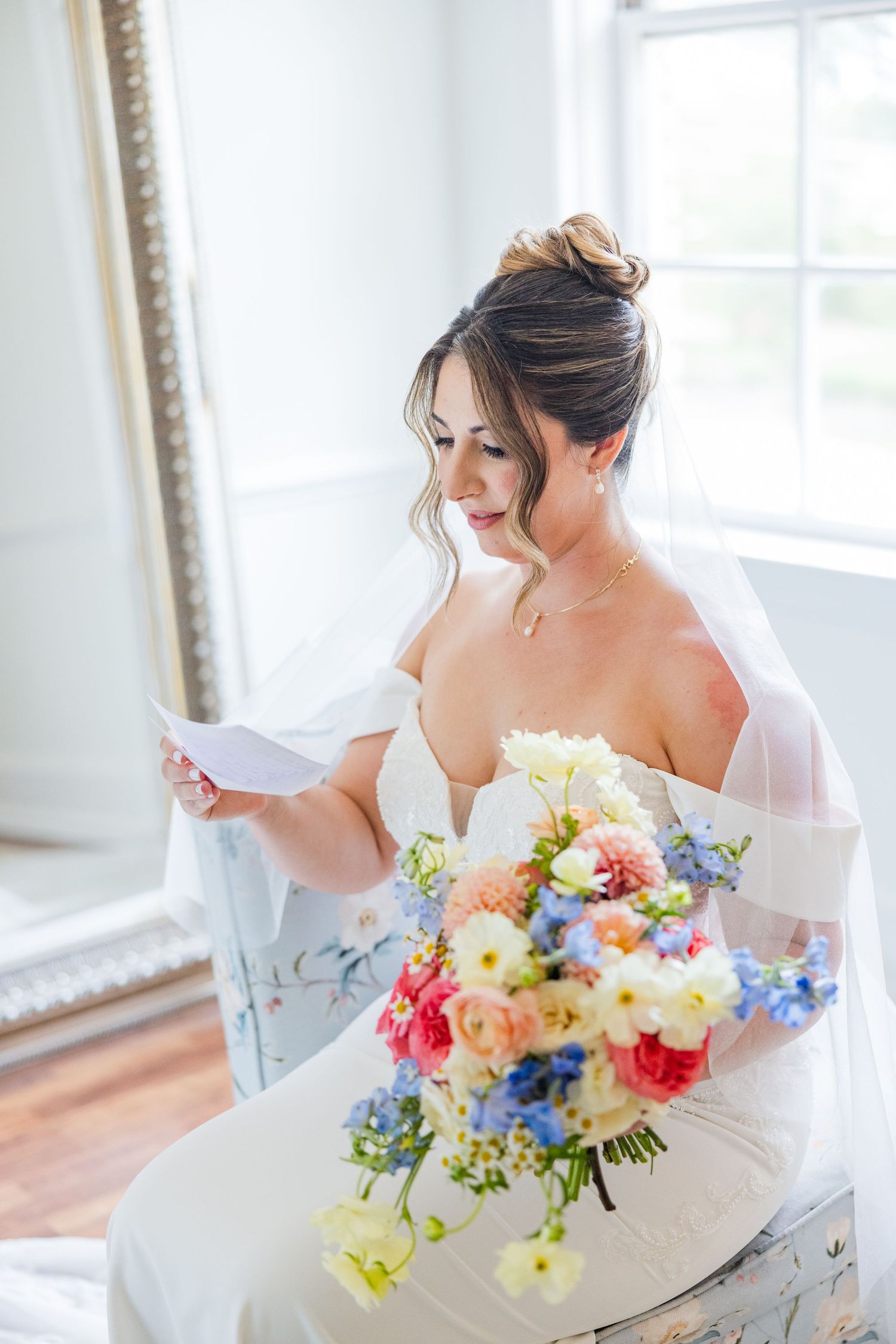 A bride in a white gown poses with a vibrant bouquet of yellow, pink, and blue flowers.