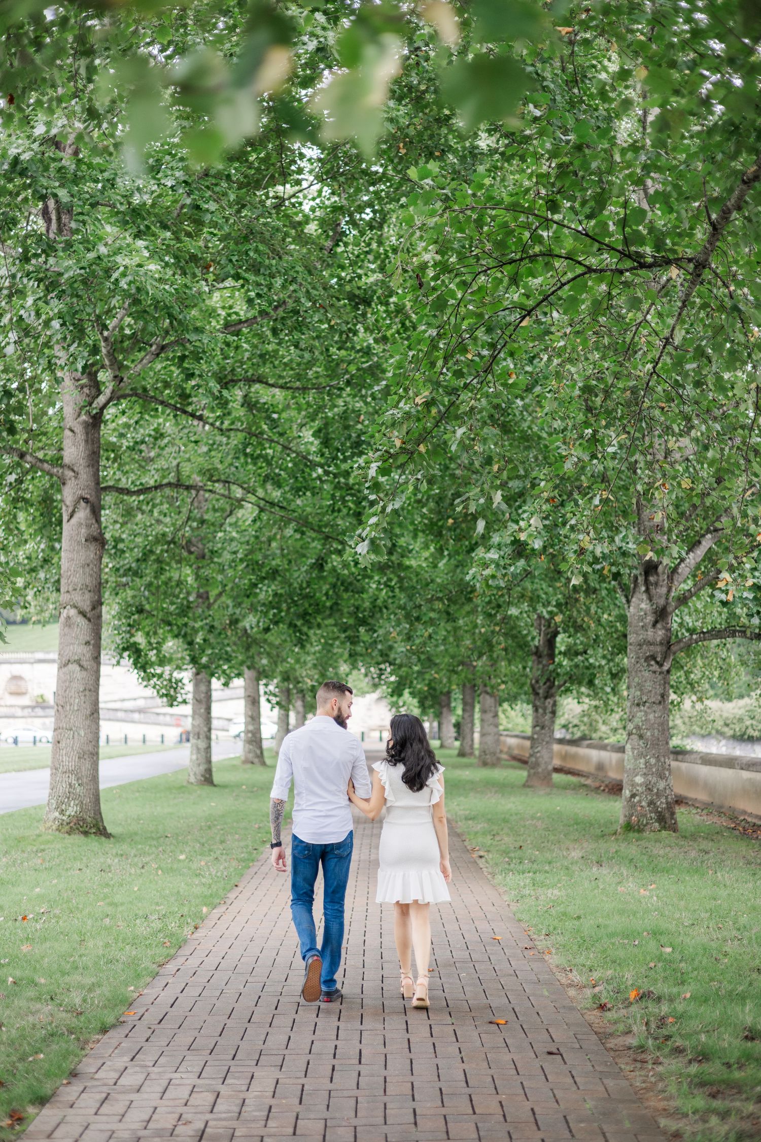 Couple walks together on brick pathway through serene tree-lined park.