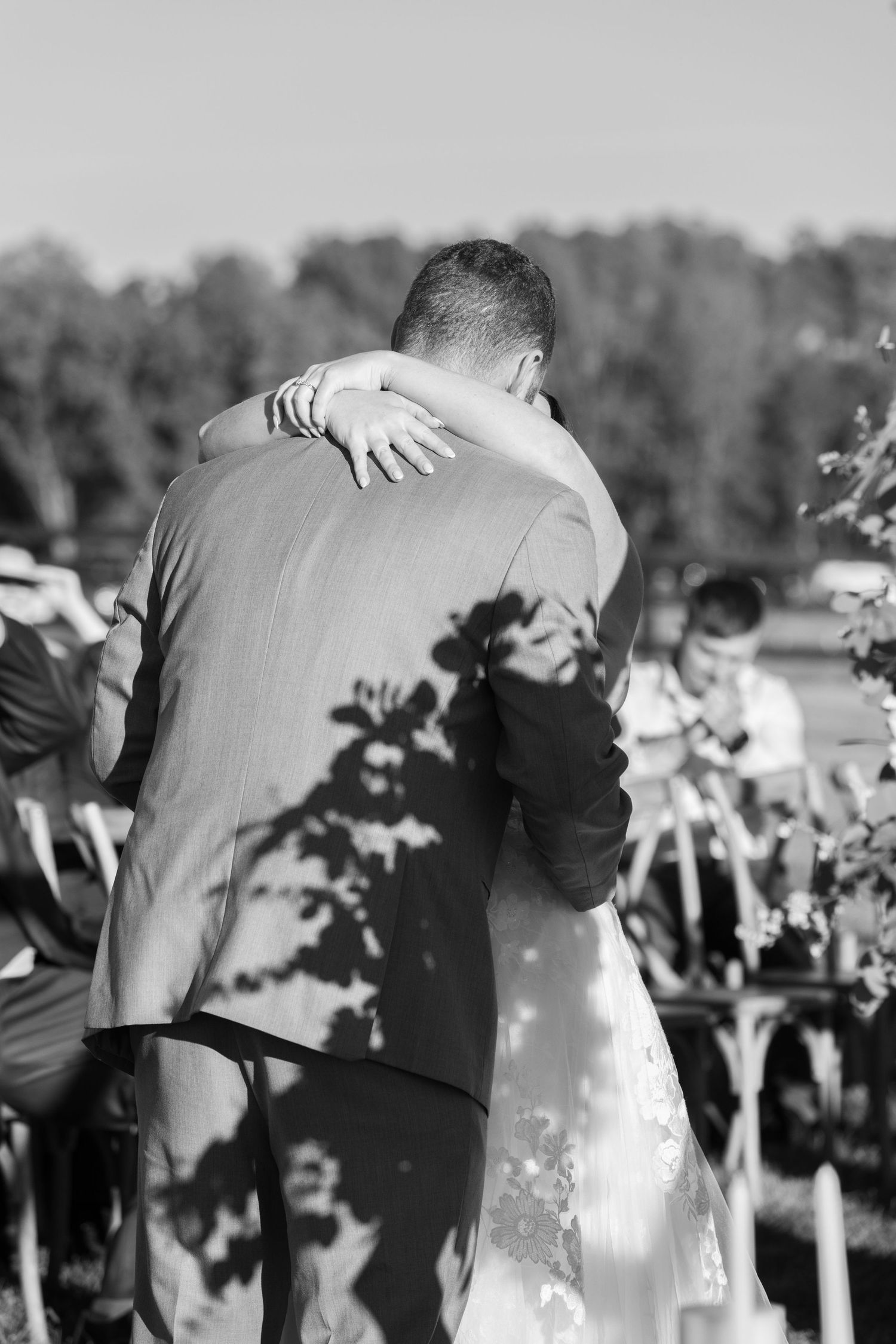 Black and white silhouette of wedding couple embracing during an outdoor ceremony.