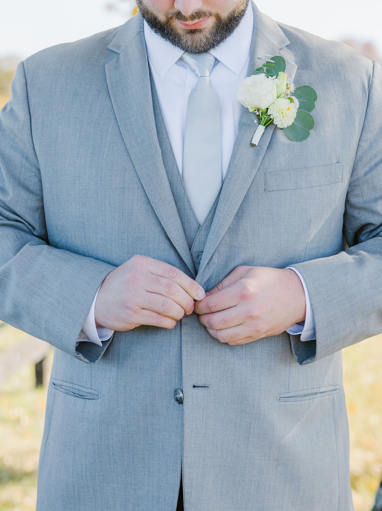 Close-up details of a light grey suit with white boutonniere and tie.