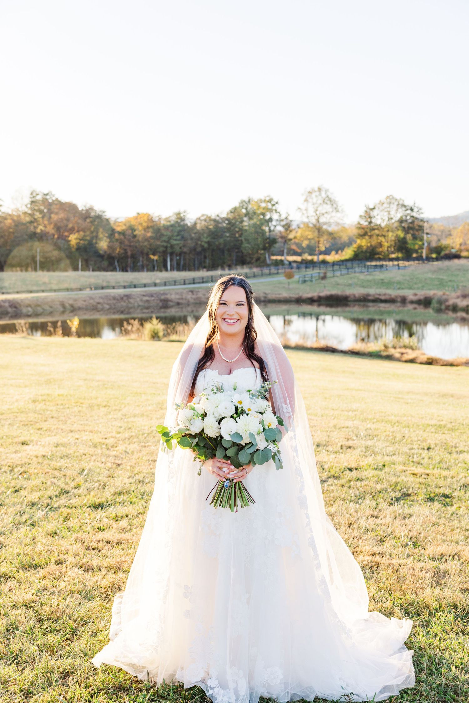 Bridal portraits in a white wedding gown holding a bouquet in a sunlit field.
