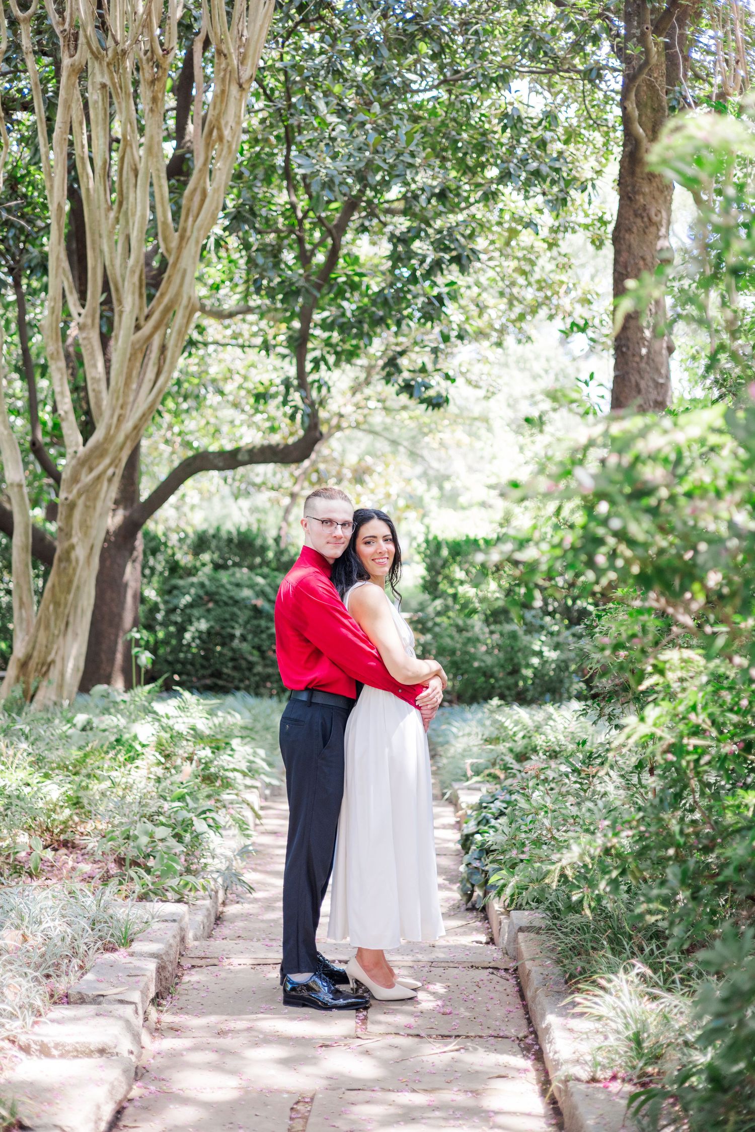 A couple embraces on a tree-lined garden path during a romantic photoshoot.