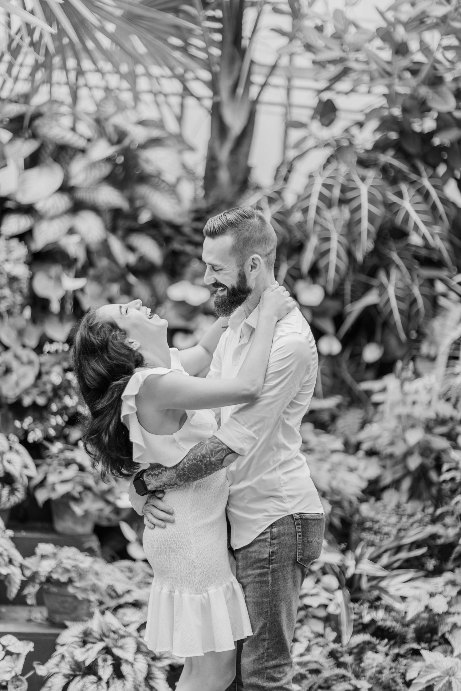 Black and white photo of a romantic embrace among tropical foliage.