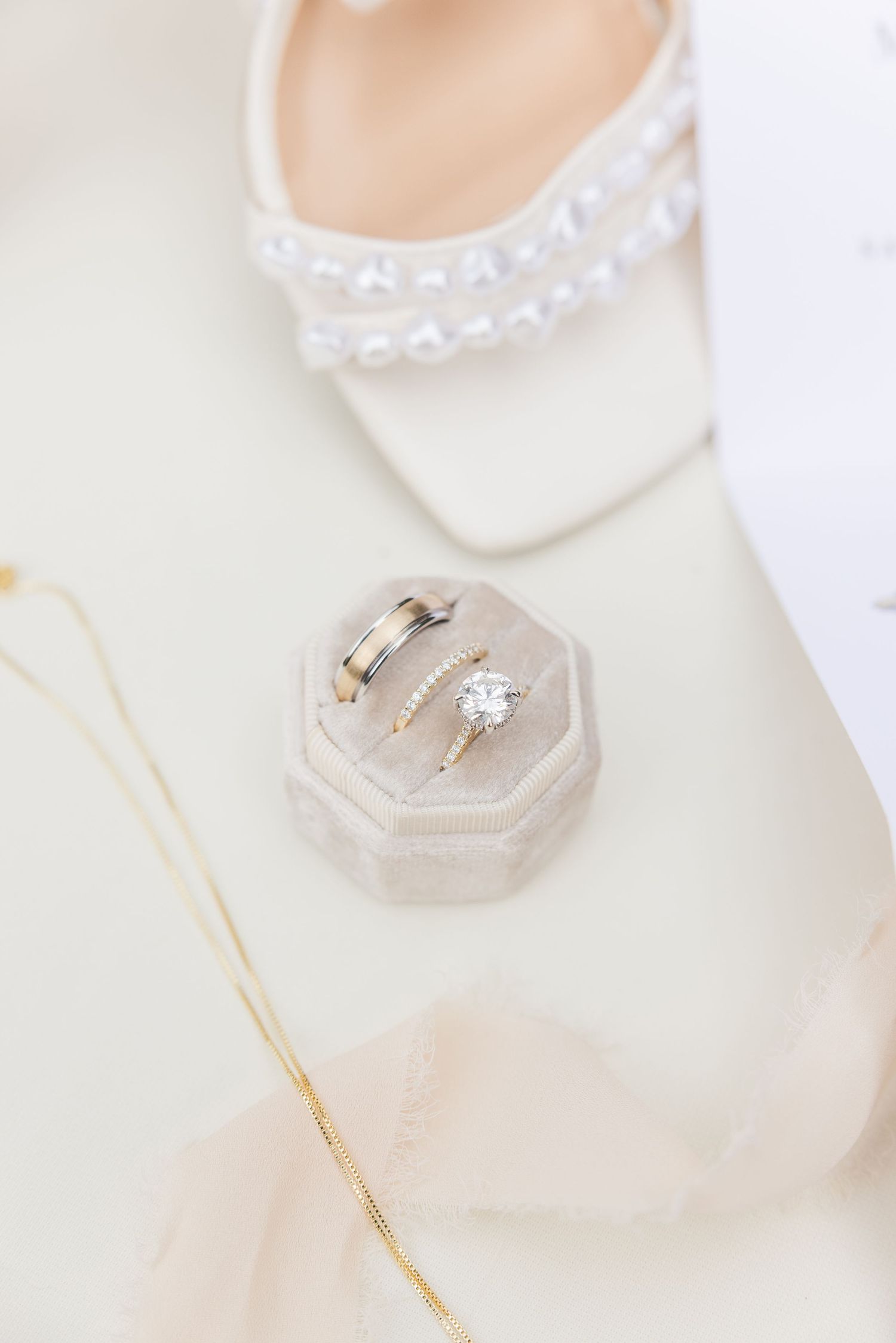 Elegant wedding accessories including delicate lace heels and diamond engagement rings on a light neutral background.