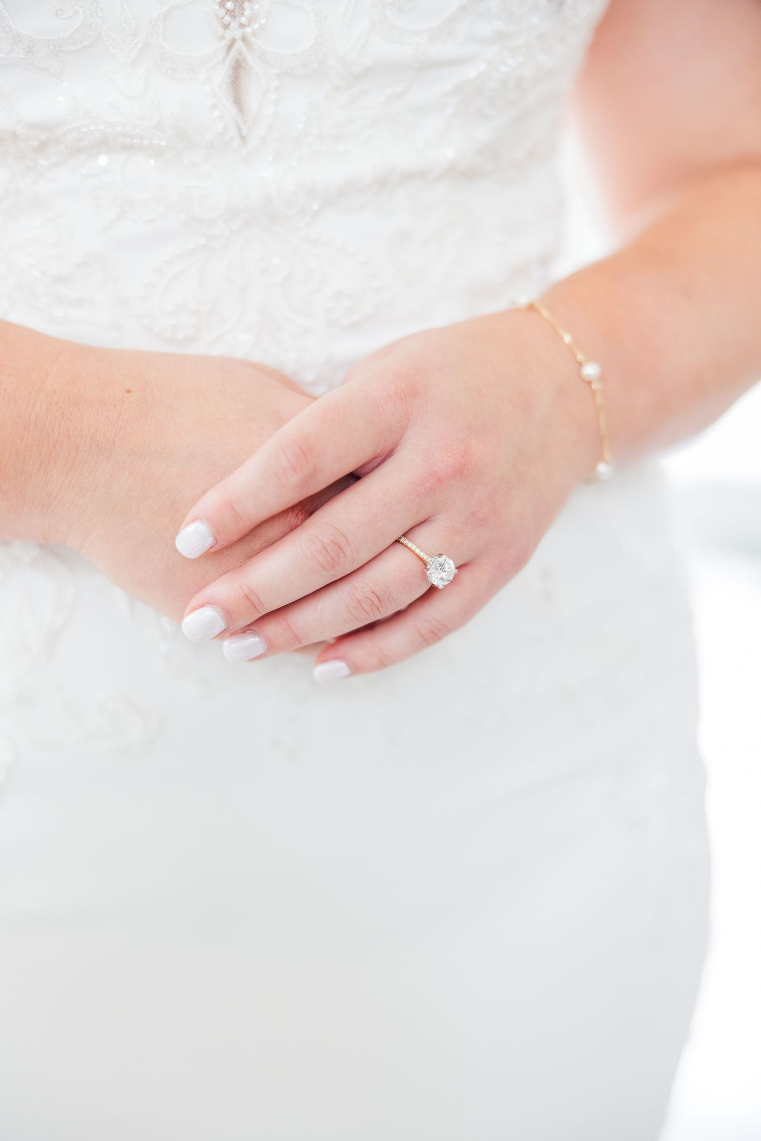Close-up of delicate white lace details and manicured hands on wedding dress.