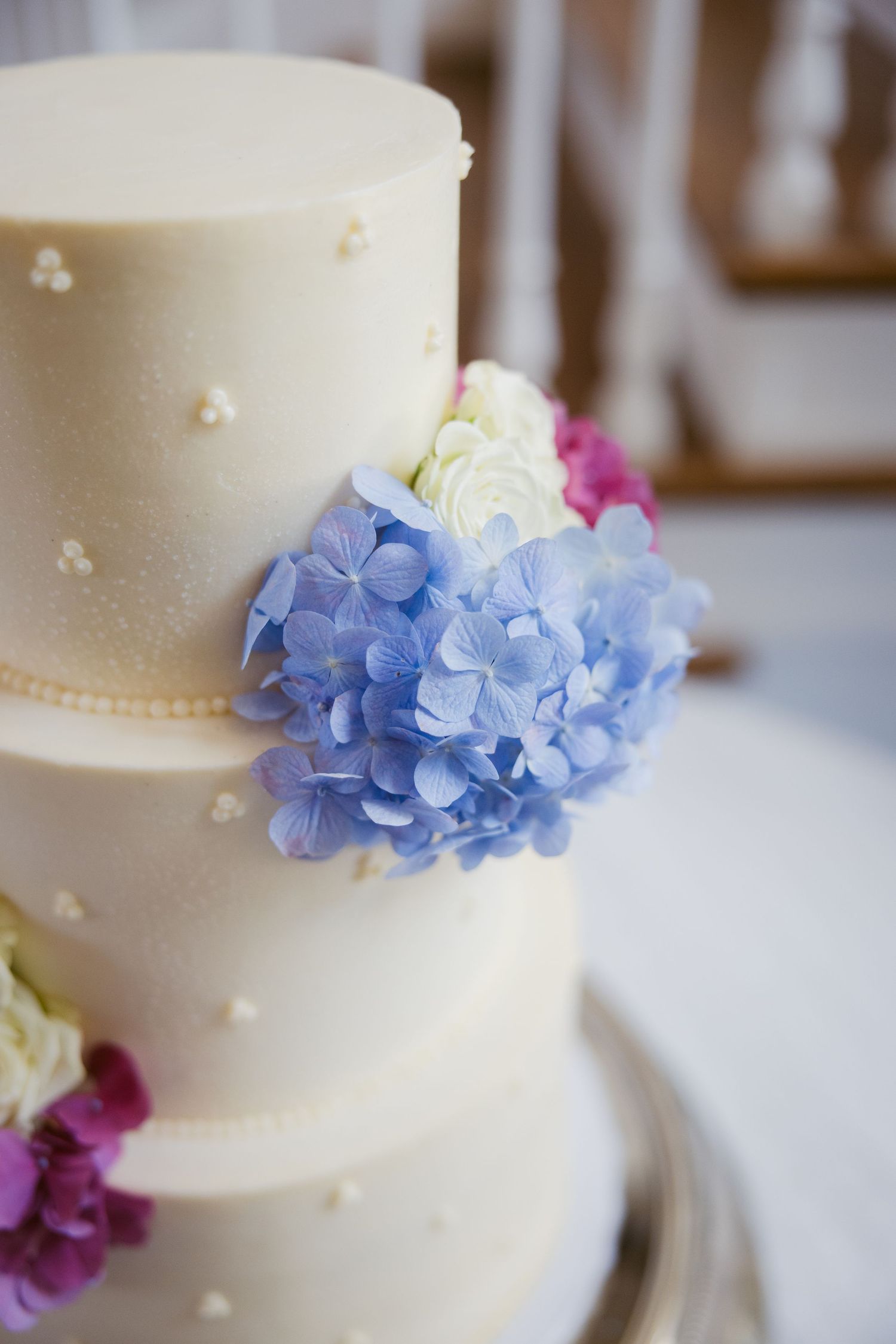 White wedding cake decorated with delicate blue hydrangea flowers and small pearl details.