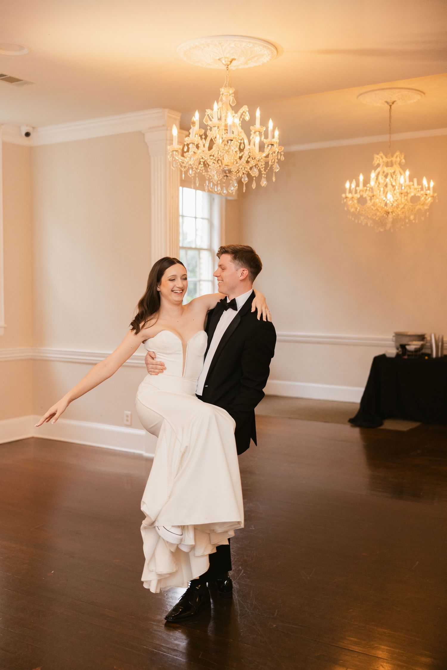 A couple dancing in an elegant ballroom with crystal chandeliers and hardwood floors.