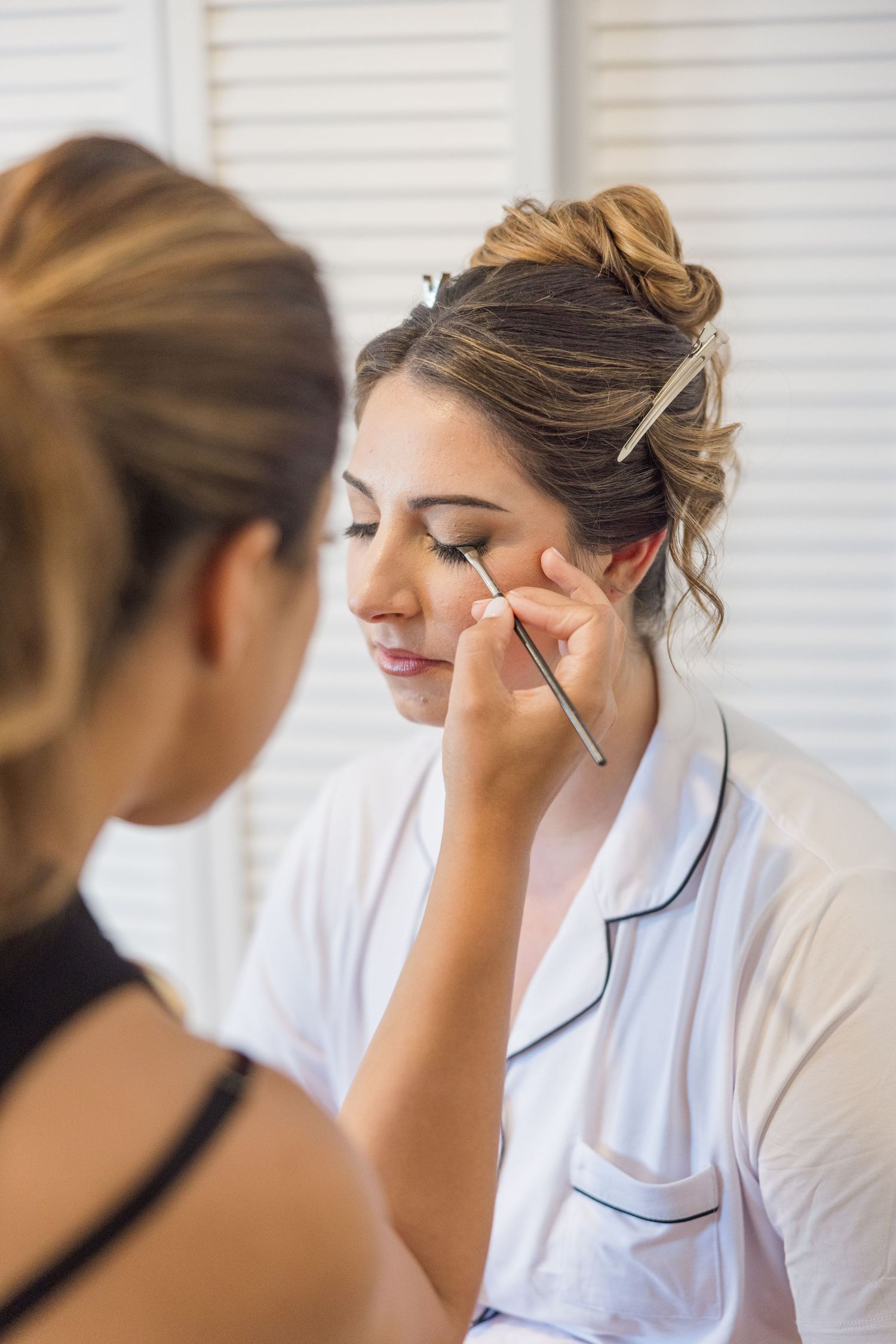 A makeup artist applies eye makeup during a wedding preparation session in a bright room.