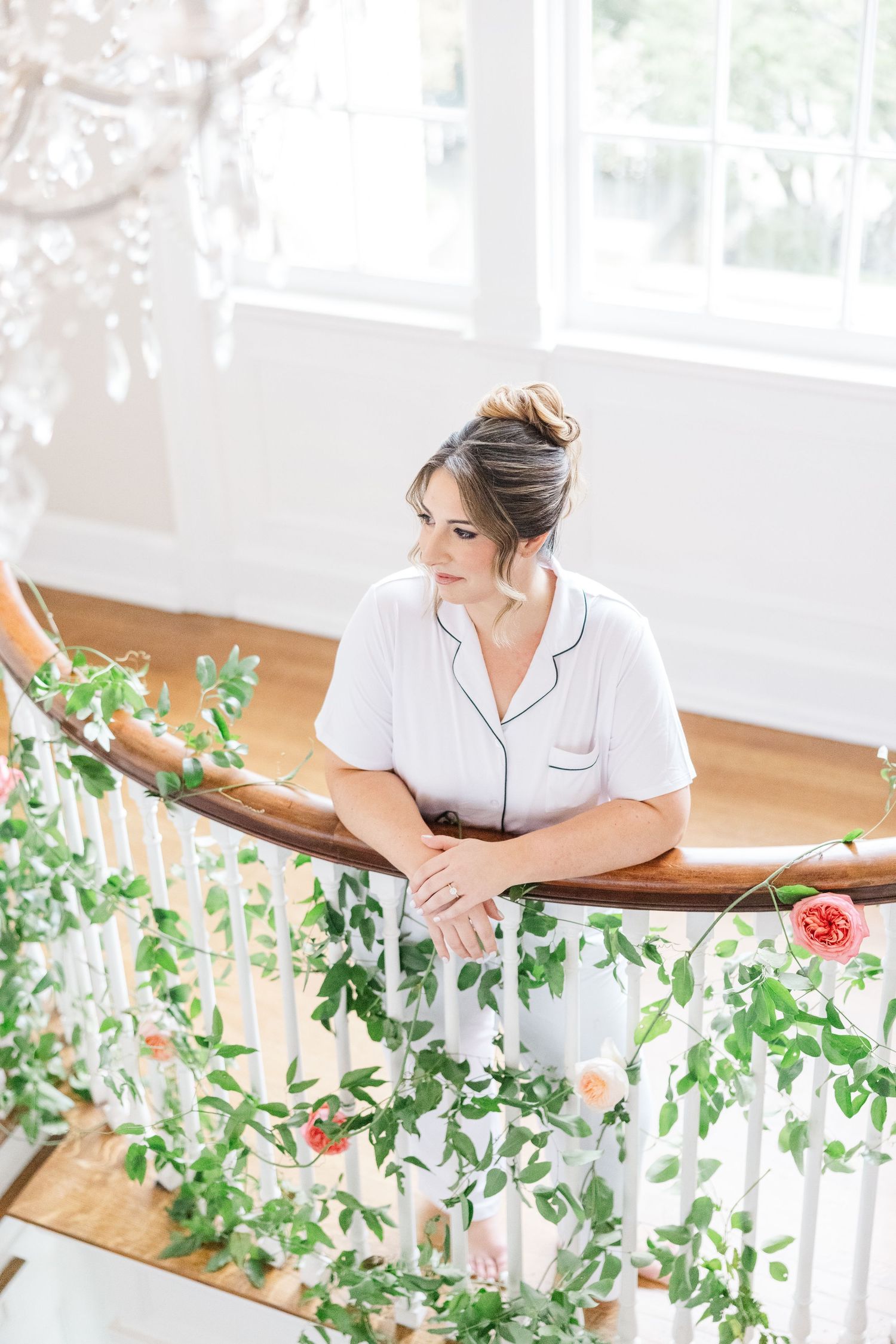 Woman in white uniform arranges fresh eucalyptus branches on wooden table near bright windows.