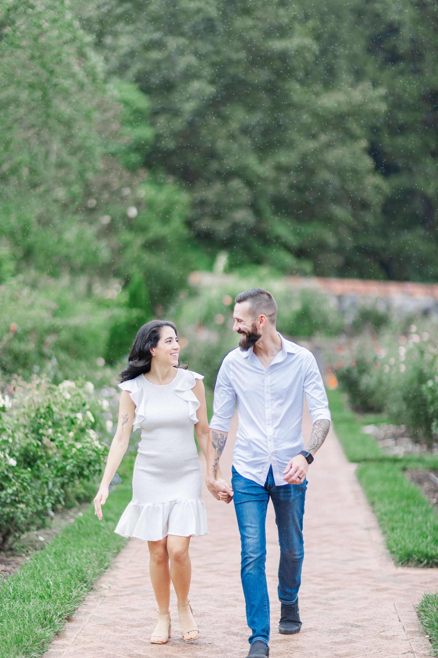 A couple walks and plays together on a garden path surrounded by lush greenery on a sunny day.
