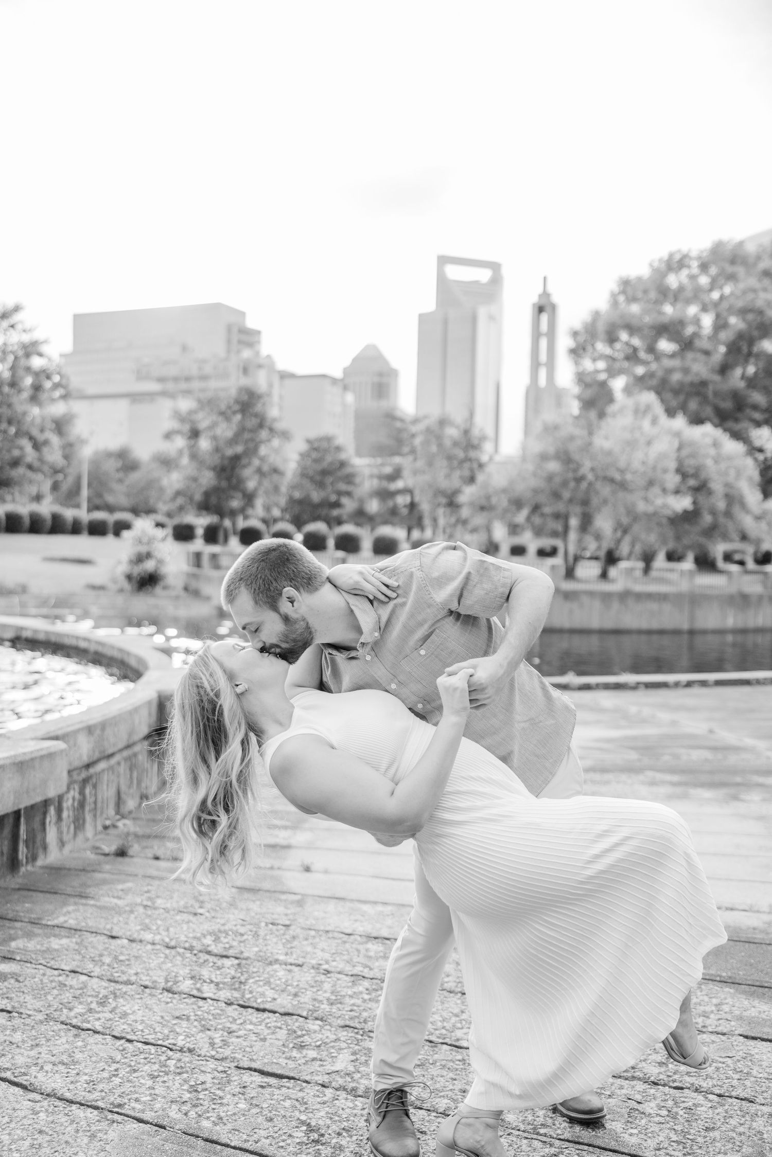 Couple performs dramatic dip pose during romantic photoshoot with urban skyline backdrop.